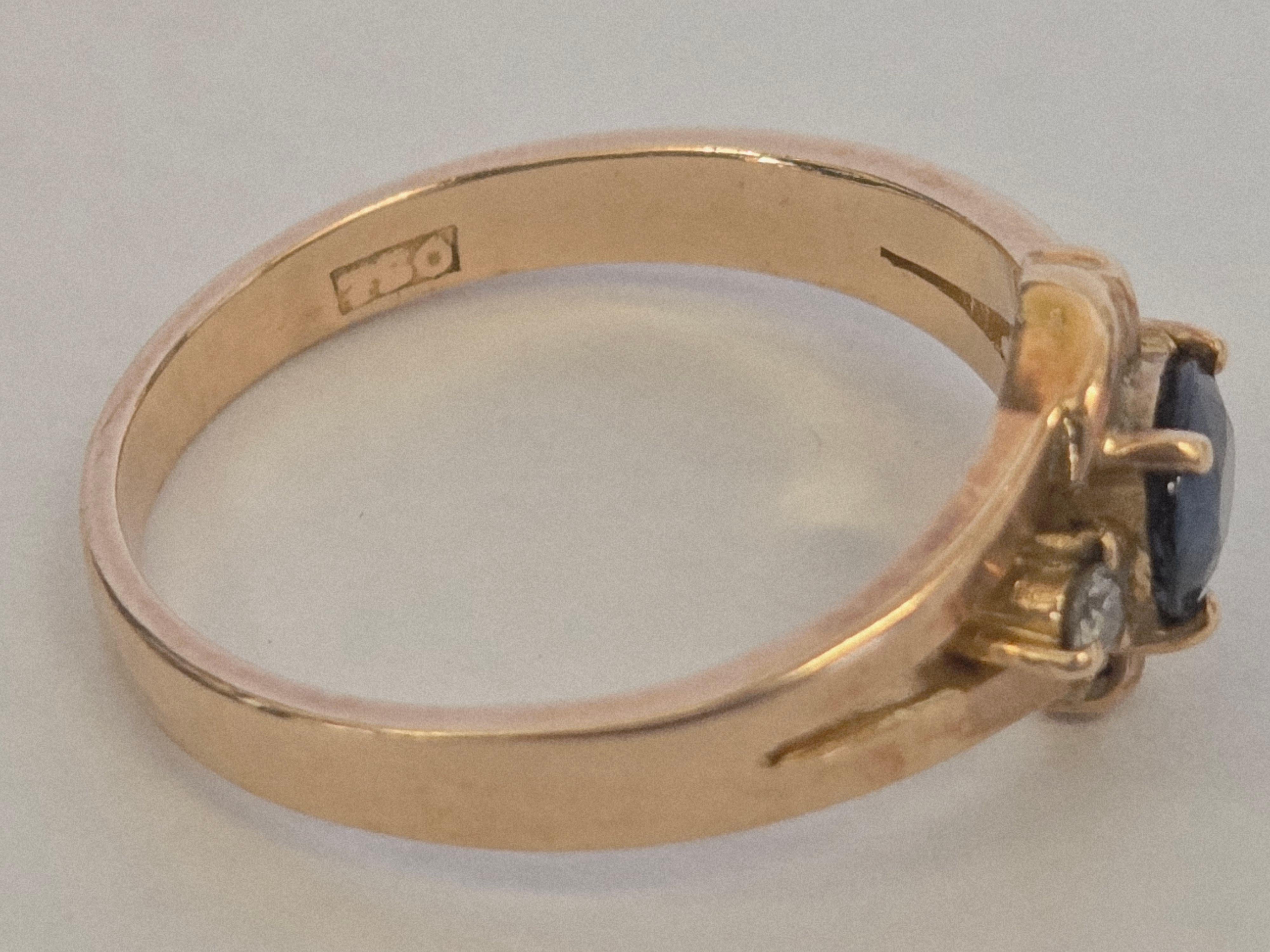 Cette élégante bague présente en son centre un saphir bleu naturel, entouré de deux diamants et serti dans une monture en or 18 carats, avec une taille de bague d'environ 5,5.