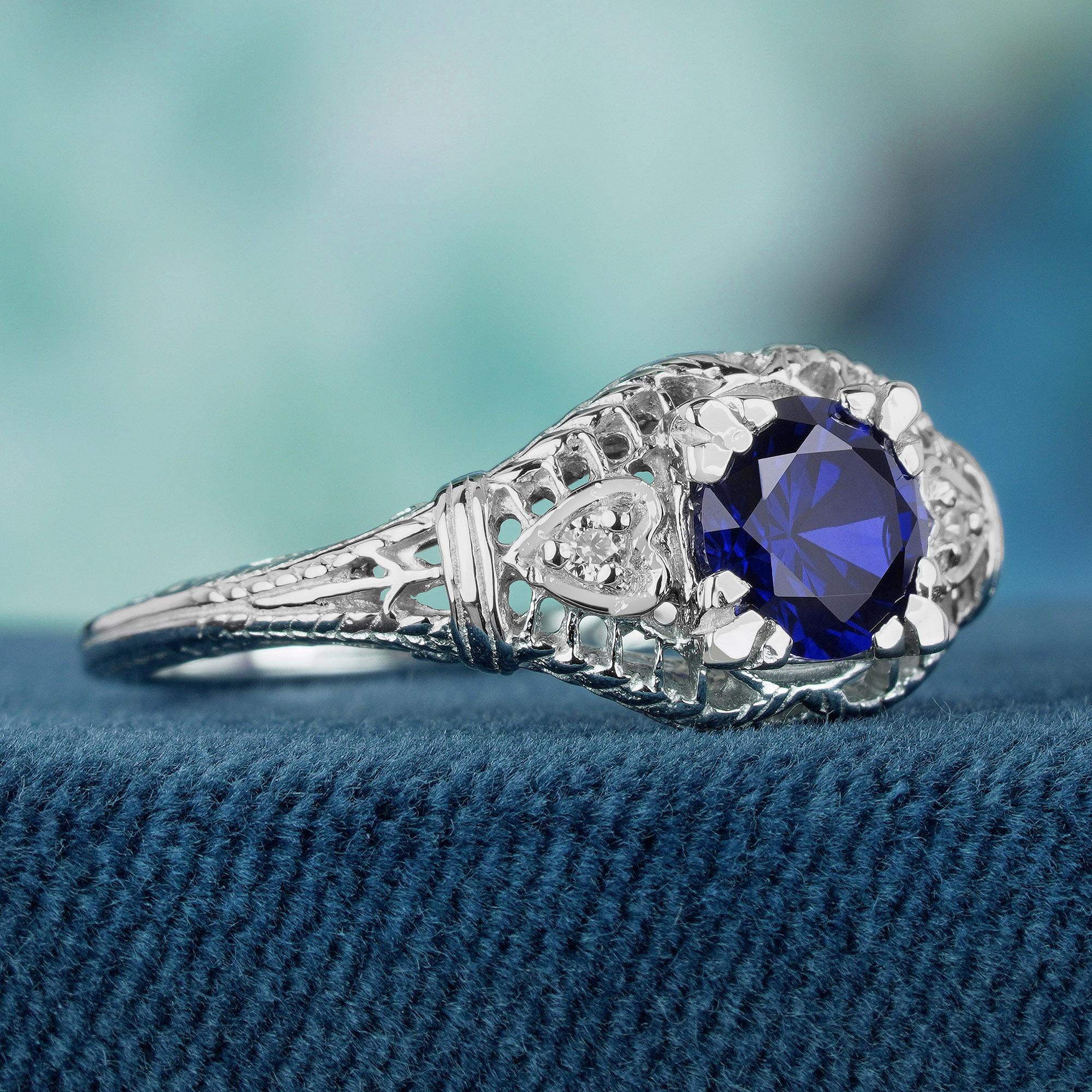 Crafted from luminous white gold with a delicate milgrain finish, this enchanting ring boasts a captivating natural blue sapphire at its core, accented by glistening diamonds. Intricate filigree detailing adorns the band, evoking a timeless vintage