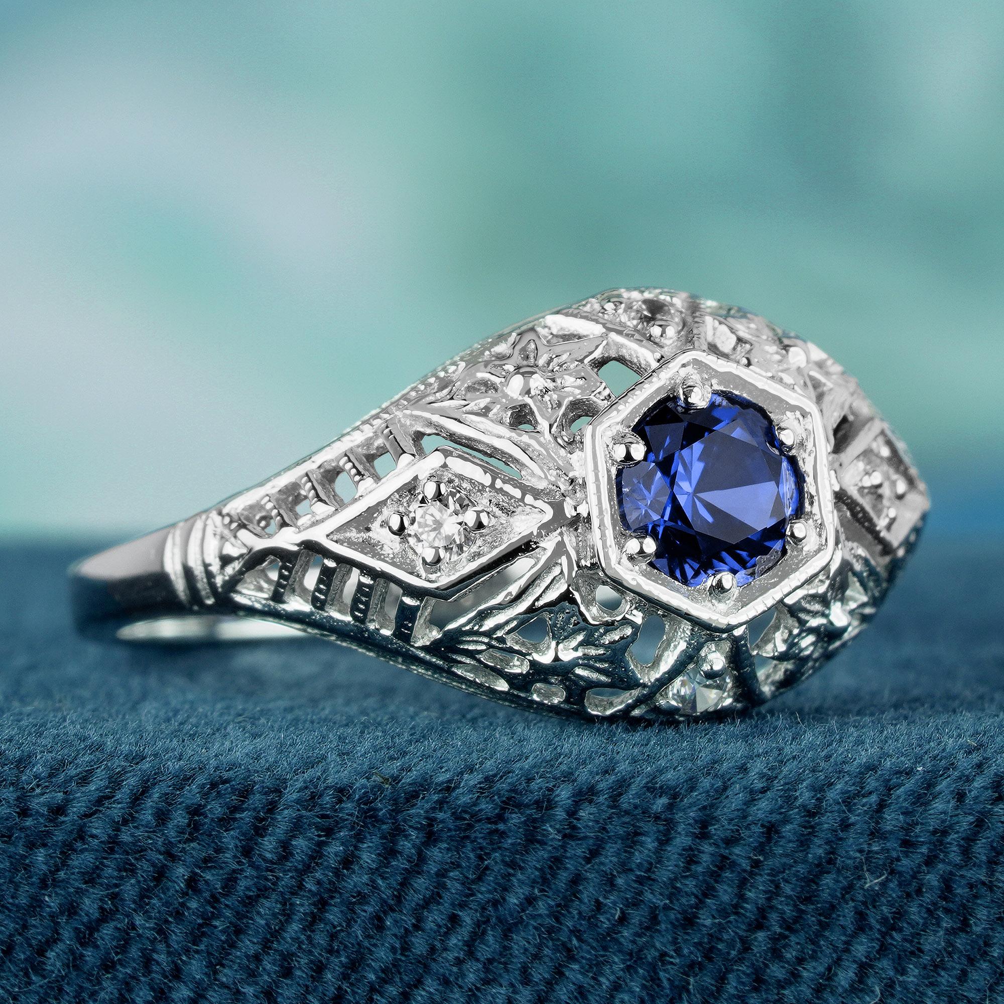 This vintage-inspired ring features a stunning natural blue sapphire as its centerpiece. The sapphire is surrounded by intricate filigree detailing in solid white gold, and multiple small diamonds add a touch of sparkle. The ring is reminiscent of