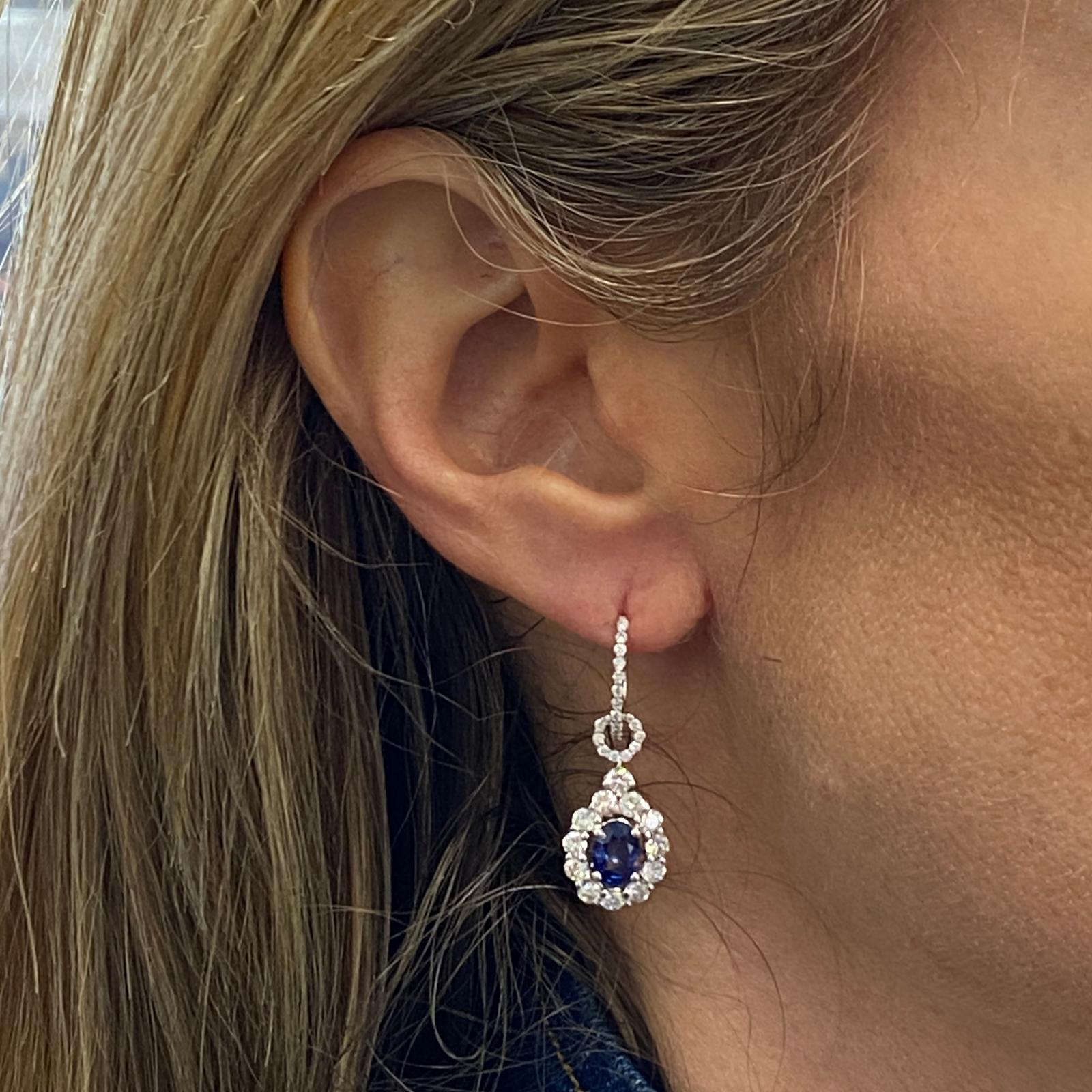 Blue sapphire diamond drop earrings fashioned in 18 karat white gold. The two matching round natural blue sapphires weigh 2.60 carats. The sapphires are surrounded by 72 round brilliant cut diamonds weighing 1.42 carat total weight and graded G-I