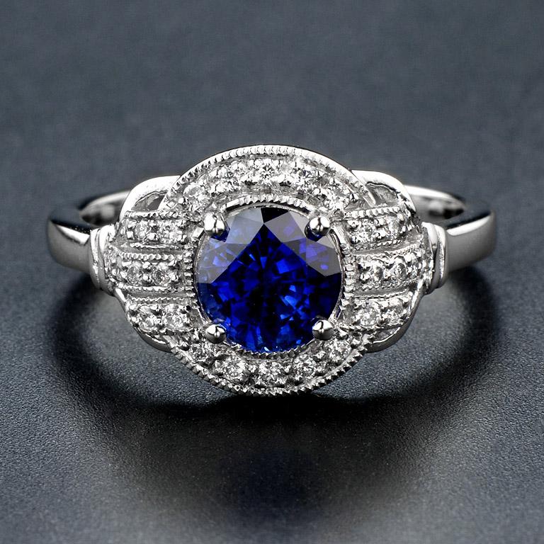 A sapphire ring with diamonds. An exquisite round Ceylon sapphire, weighing 1.25 carats, is set into 18k white gold and accentuated by a halo of diamonds, with additional diamonds set into the shoulders. 
Sapphires have been long associated with