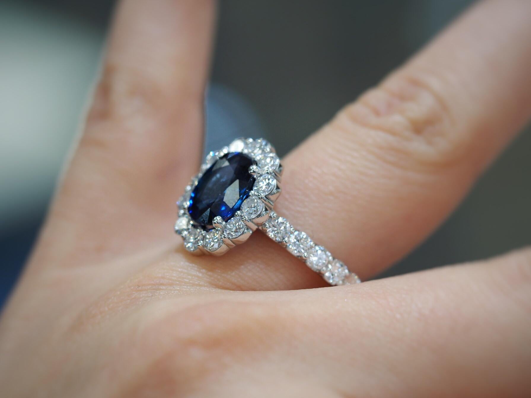 Stunning 2.09CT AGL Certified blue sapphire is set in a diamond flower halo setting flowing with 1.72ctw round brilliant cut diamonds on the halo and down the shank set in 18K white gold. Can have sized up or down prior to shipping at no additional