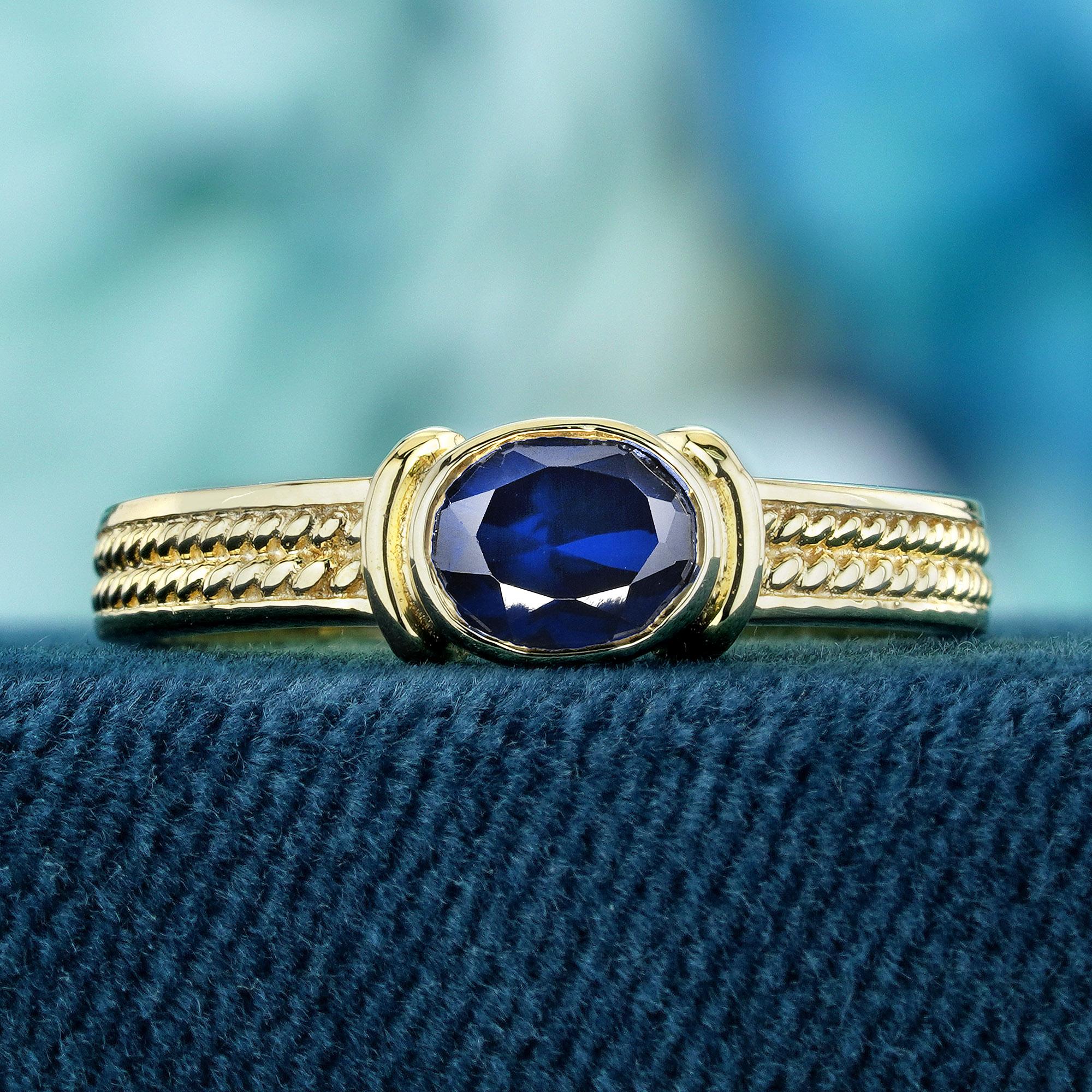 This vintage-style solitaire ring showcases a single, oval-shaped blue sapphire nestled in a bezel setting on a yellow gold band adorned with intricate milgrain details. With its classic and elegant design, this ring is a captivating piece of