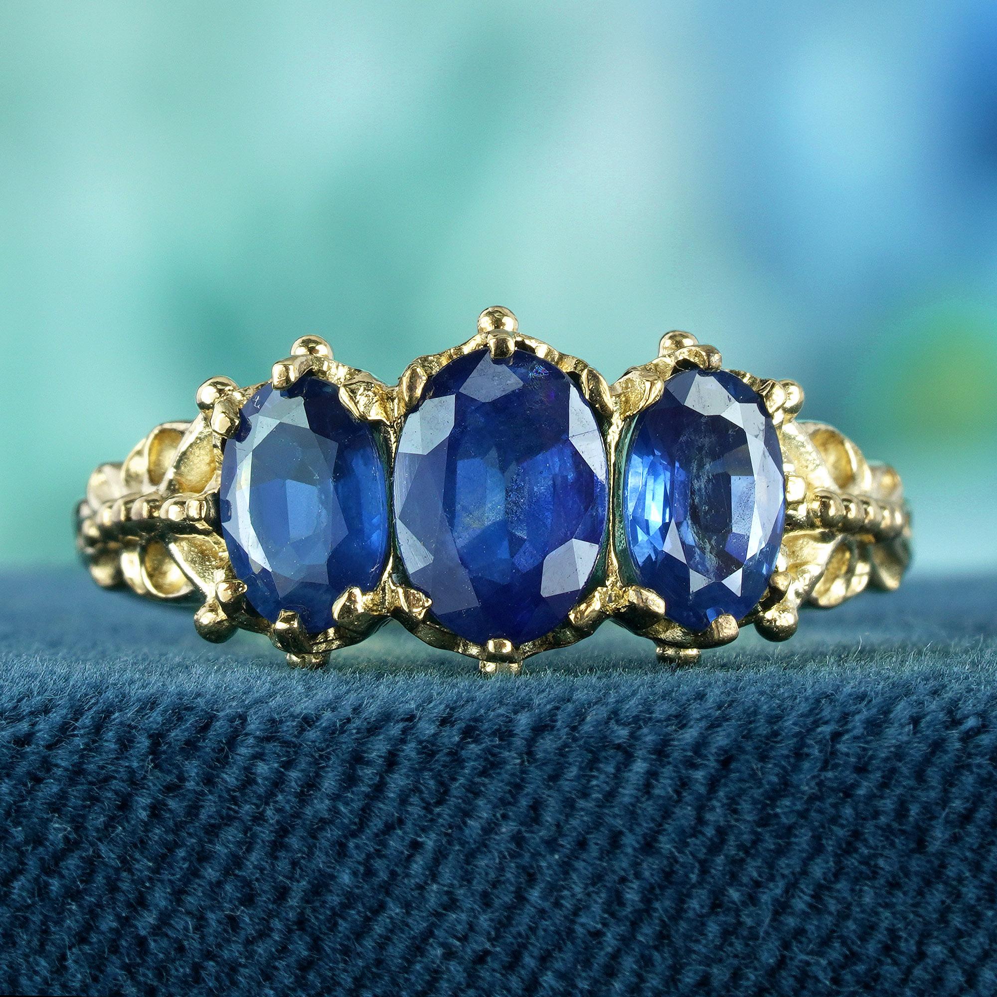 Dieser Ring zeigt drei natürliche blaue Saphire, jeder mit einem fesselnden tiefblauen Farbton und einem facettierten Ovalschliff, der dafür sorgt, dass sie das Licht einfangen und die Blicke auf sich ziehen. Das filigrane Band aus Gelbgold strahlt