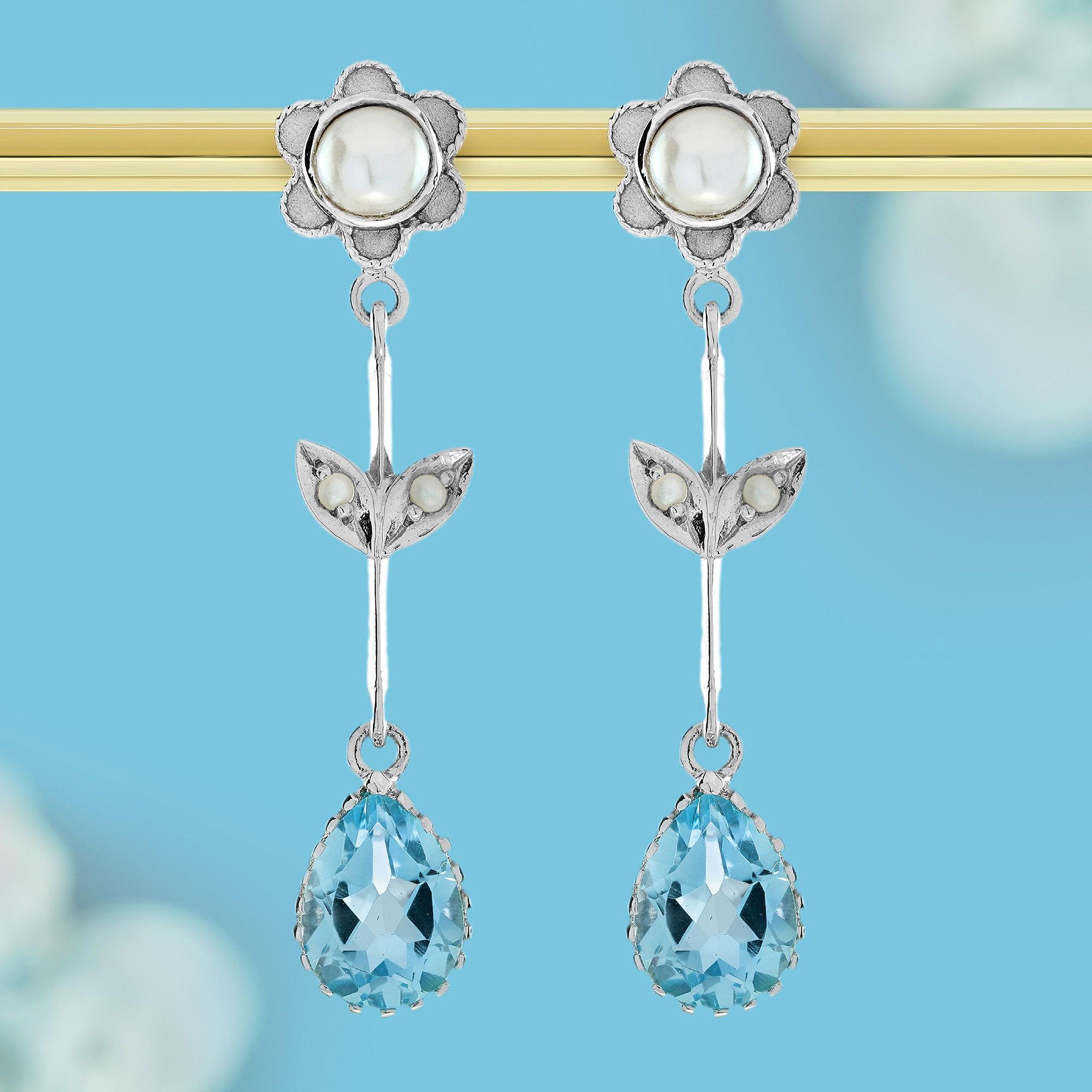 Adorn yourself with the timeless elegance of these vintage-inspired floral earrings. Featuring stunning blue topaz that dangles gracefully below lustrous white pearls, set at the heart of the intricate flower and leaf design, these earrings