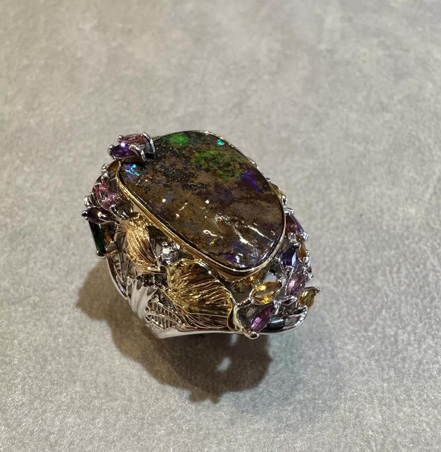 Natural Boulder Opal and Mixed Gem Ring in 18k Multitone Gold and Platinum

Boulder Opal and Gemstone Ring features a center Boulder Opal with Brown background and flashes of Orangy Red-Green-Blue accented with a mix of color semi-precious stones
