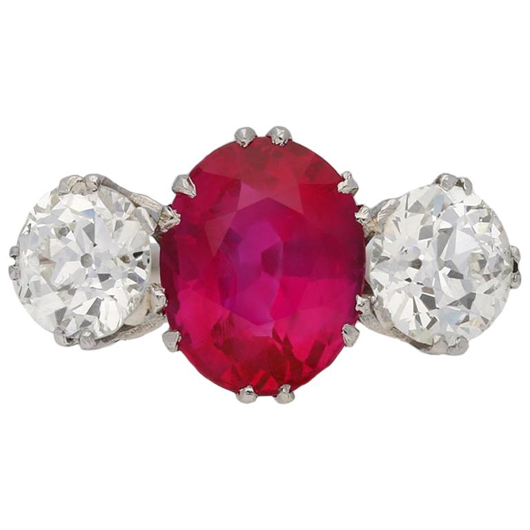 Natural Burmese ruby and diamond ring. Set with an oval old cut natural unenhanced Burmese ruby to centre in an open back claw setting with an approximate weight of 3.41 carats, flanked by two round old cut diamonds in open back claw settings with