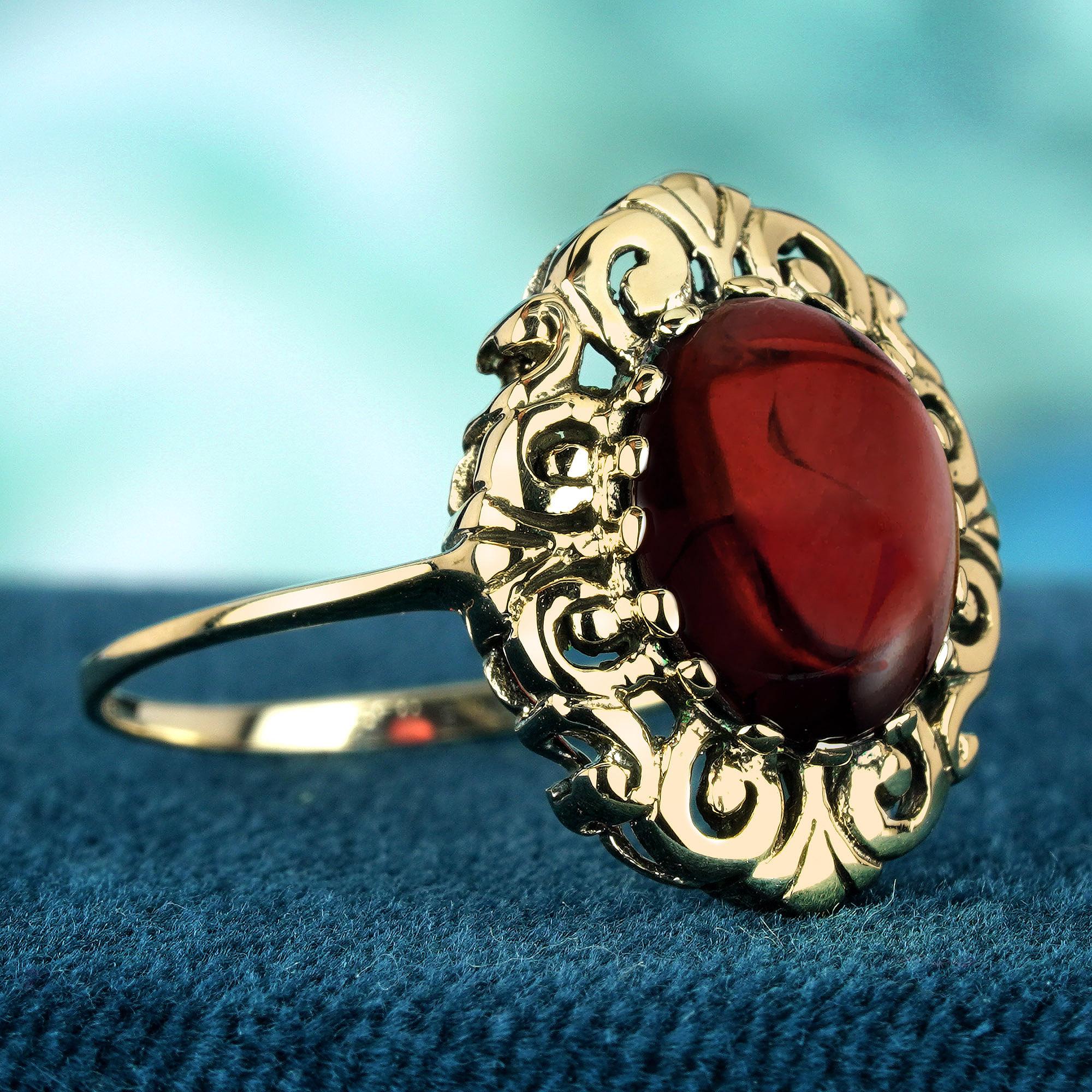 This vintage-inspired ring’s centerpiece is an oval cabochon-cut natural garnet, known for its deep red hue and smooth, domed surface. This cabochon garnet is set amidst a backdrop of yellow gold, which is adorned with intricate vintage-style