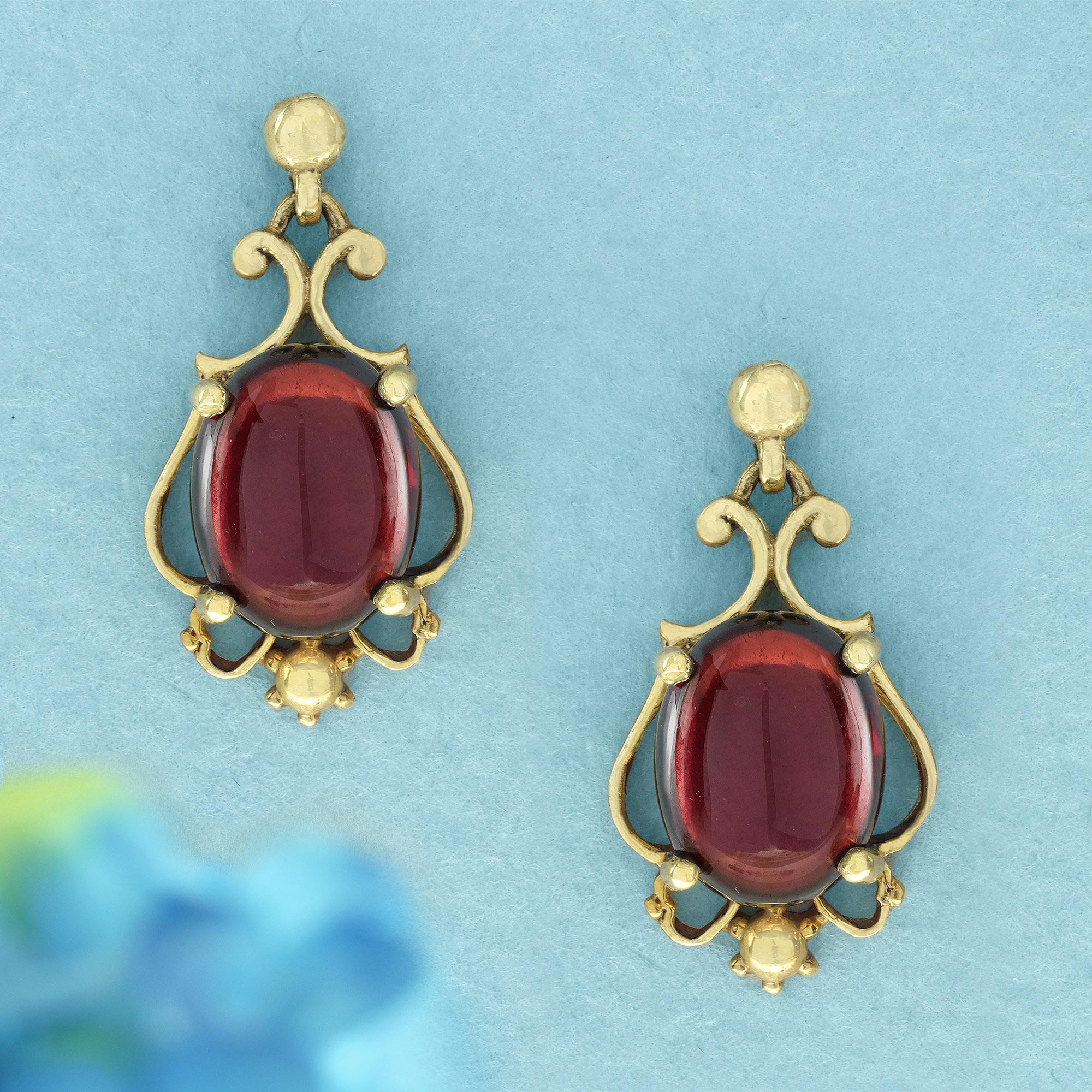 Indulge in timeless elegance with these vintage-inspired garnet earrings. Each earring features a captivating round, cabochon-cut garnet, its deep red color catching the light with a smooth, polished brilliance.  Set in a beautiful scrollwork gold