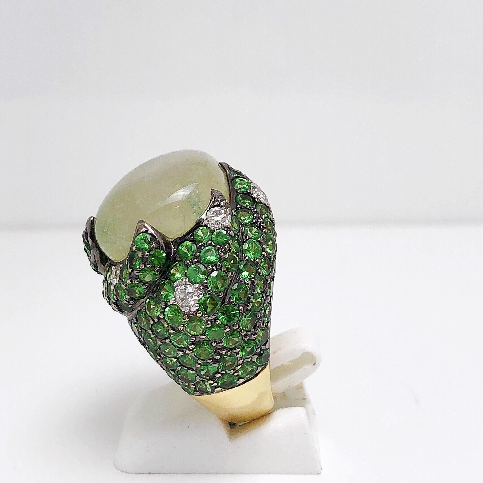 A large organic shaped cabochon natural tsavorite is surrounded by 167 round brilliant tsavotires and diamonds in a dramatic 6 pronged raised setting. The ring is 18 -karat yellow gold and the stones are set in blackened 18- karat gold to add to the