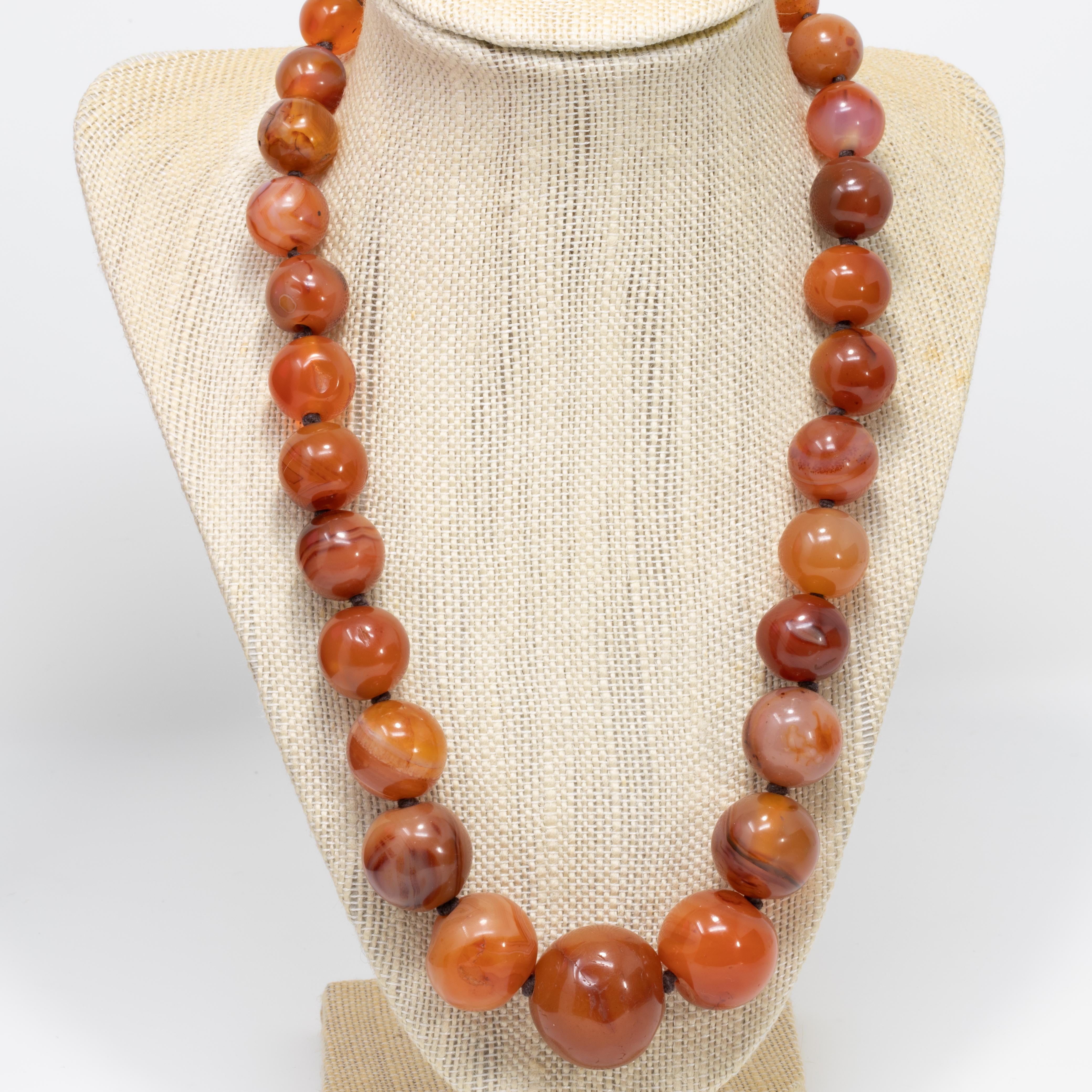 An extravagant carnelian graduated bead necklace on a dark brown knotted string. Features genuine carnelian beads ranging from 9.5mm to 25.5mm in diameter, fastened with a 16mm long 585 (14 karat) yellow gold clasp. A rich, dark orange, translucent