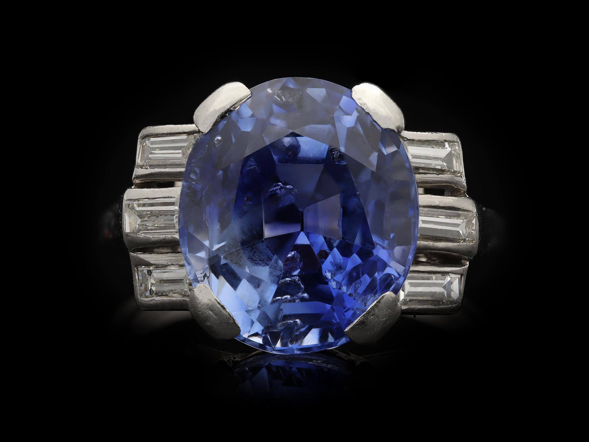 Ceylon sapphire and diamond ring. Centrally set with an oval old cut natural unenhanced Ceylon sapphire in an open back claw setting with an approximate weight of 9.30 carats, flanked by six horizontally set rectangular baguette cut diamonds in open