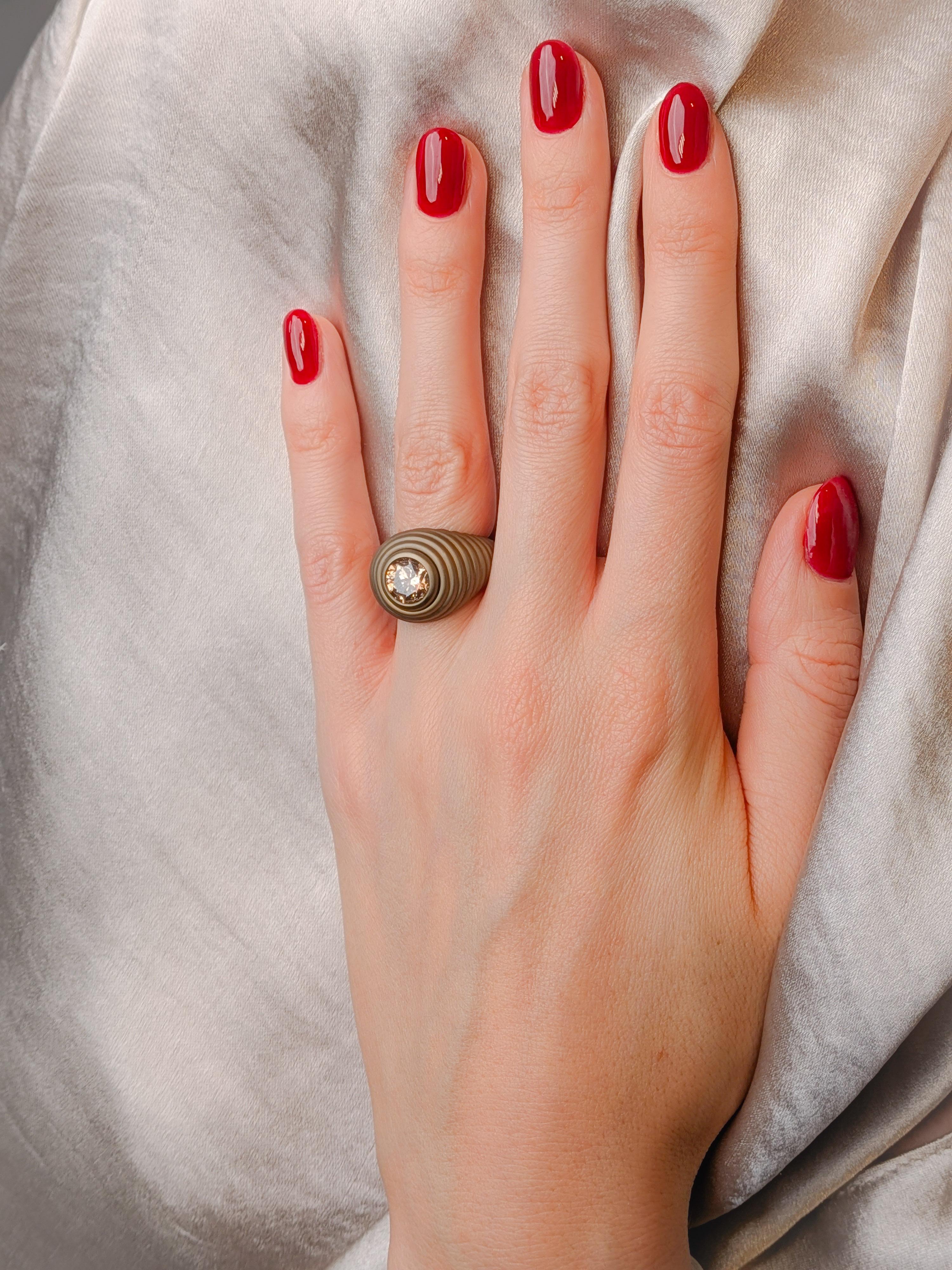 Bague en titane doré ornée d'un diamant champagne naturel et d'une pierre taillée en brillant de 2,39 carats, dont les contours sculpturaux en escalier s'inspirent des dessins d'archives de René Sim Lacaze.

Cette bague MXHM s'inscrit dans