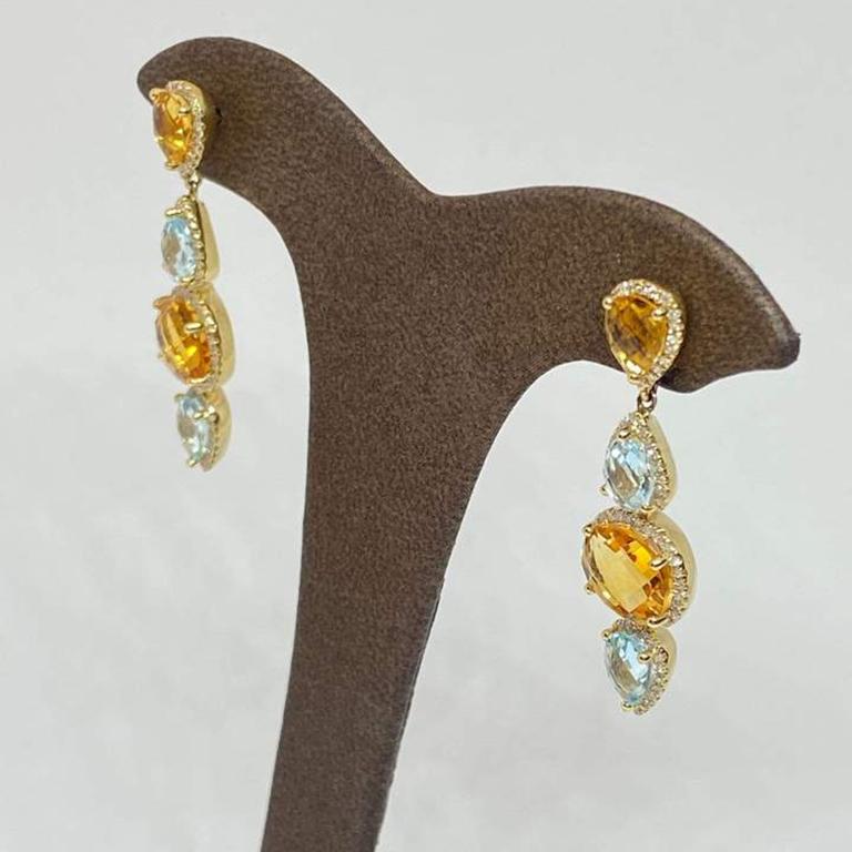 Natural golden citrine and blue topaz dangle earrings designed in 14 karat yellow gold. The gemstones are surrounded by diamond halos. The earrings have a post and friction earring back. Gemstone total weight: 6.85 carats. Diamond total weight: 0.39