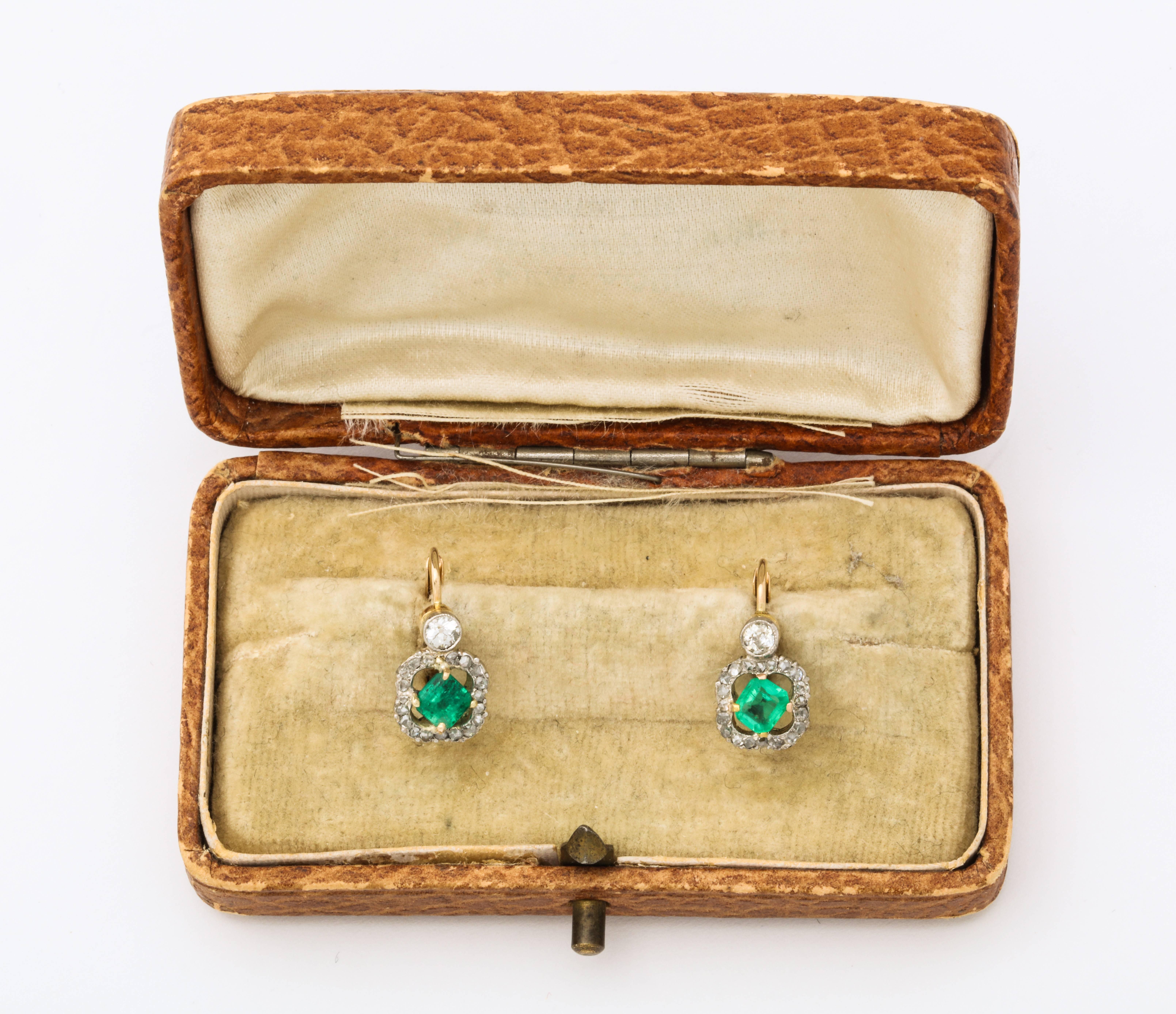 A delicate pair of natural Colombian square cut emeralds surrounded by a ring of diamonds and suspended from bezel set round diamonds in 18K gold  with lever closures.  
