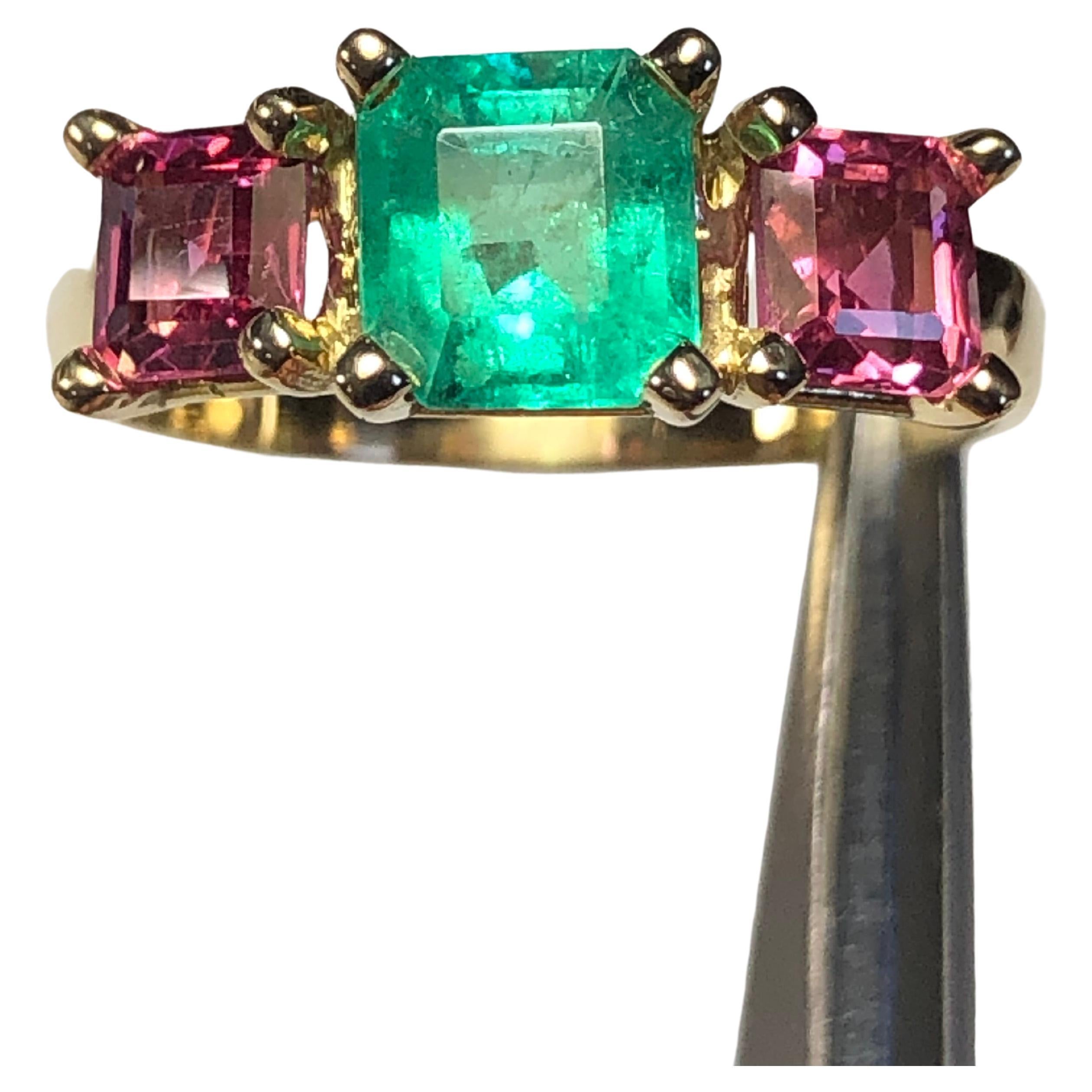 Dieser klassische Trilogie-Ring zeigt einen natürlichen mittelgrünen kolumbianischen Smaragd, flankiert von einem Paar natürlicher rosa Mahenge-Spinelle im Quadratschliff. Fassung aus 18 Karat Gelbgold. Sehr klassisch und einfach für den Alltag zu