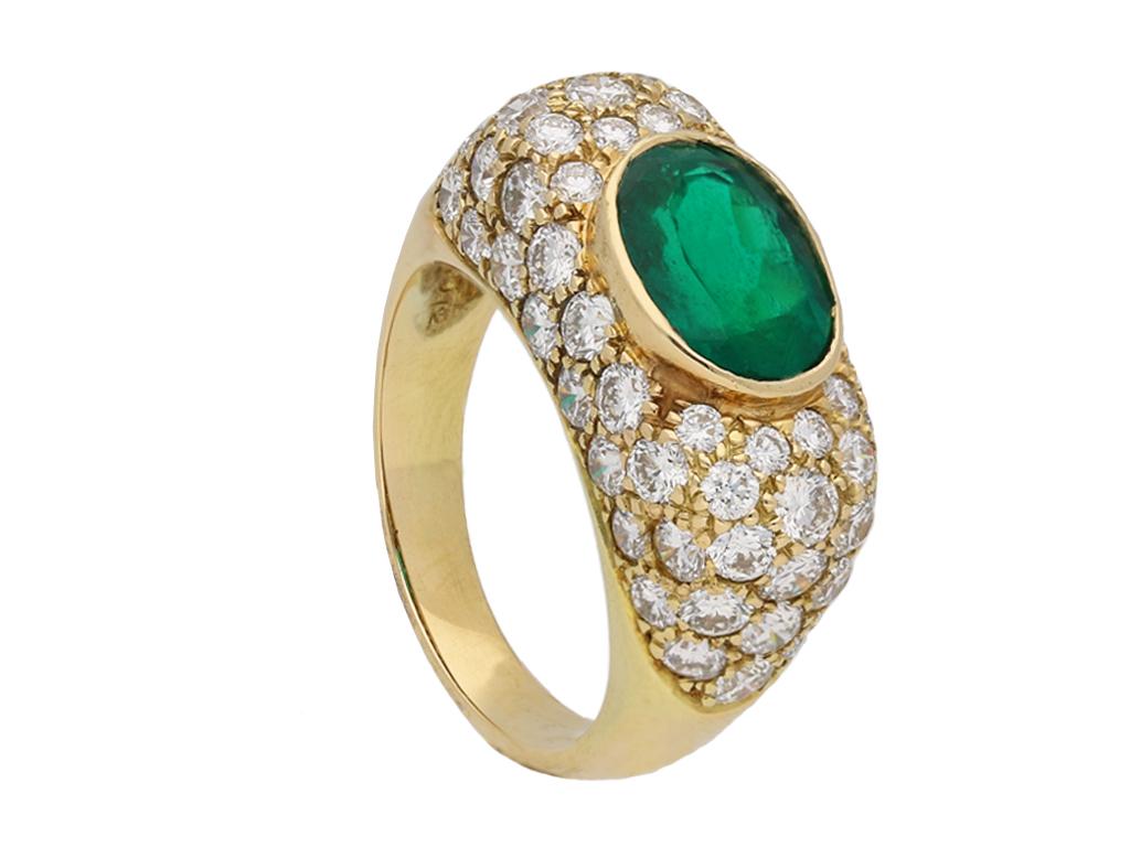 Colombian emerald and diamond cluster ring by Oscar Heyman Brothers. Horizontally set with an oval old cut natural Colombian emerald with no colour enhancement in an open back rubover setting with an approximate weight of 1.60 carats, encircled by a