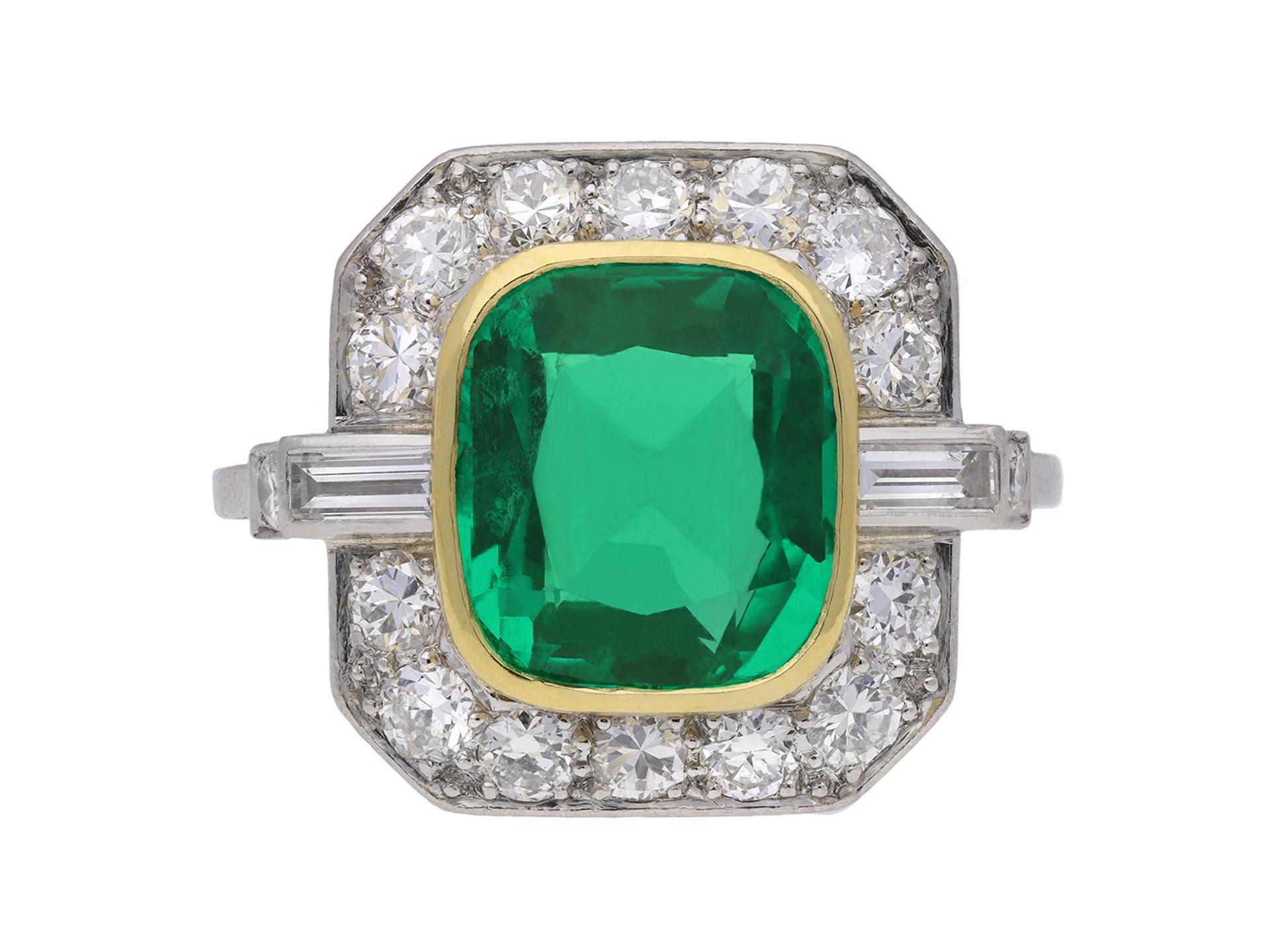 Colombian emerald and diamond cluster ring. Set with a cushion shape old cut Natural Colombian emerald with no colour enhancement in an open back yellow gold rubover setting with an approximate weight of 3.00 carats, flanked by two horizontally set