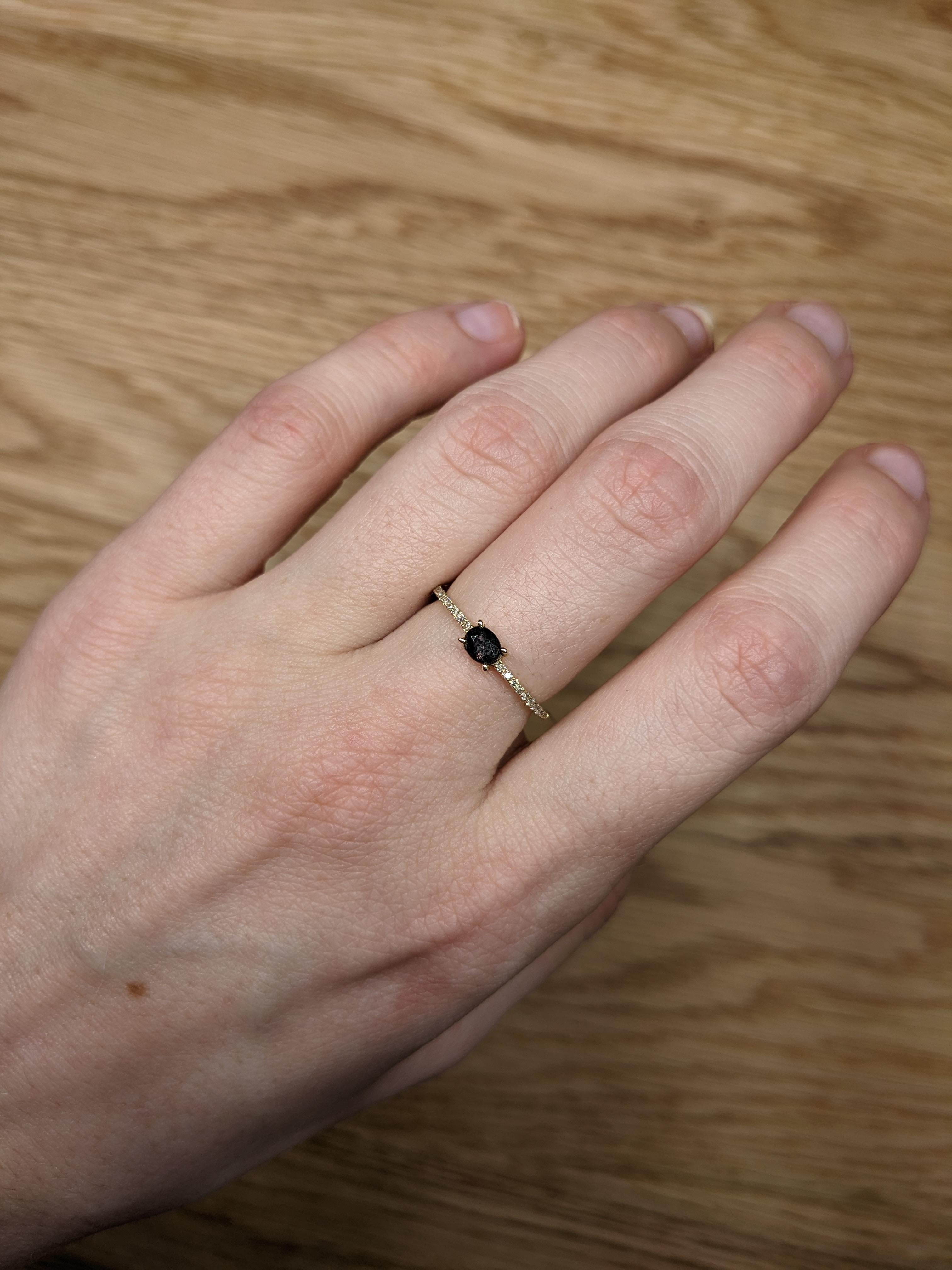 An exquisite engagement ring features a 0.32-carat oval-shaped Alexandrite gemstone, known for its remarkable color-changing properties. The stone elegantly transitions from green to red depending on the light, adding a unique and captivating aspect