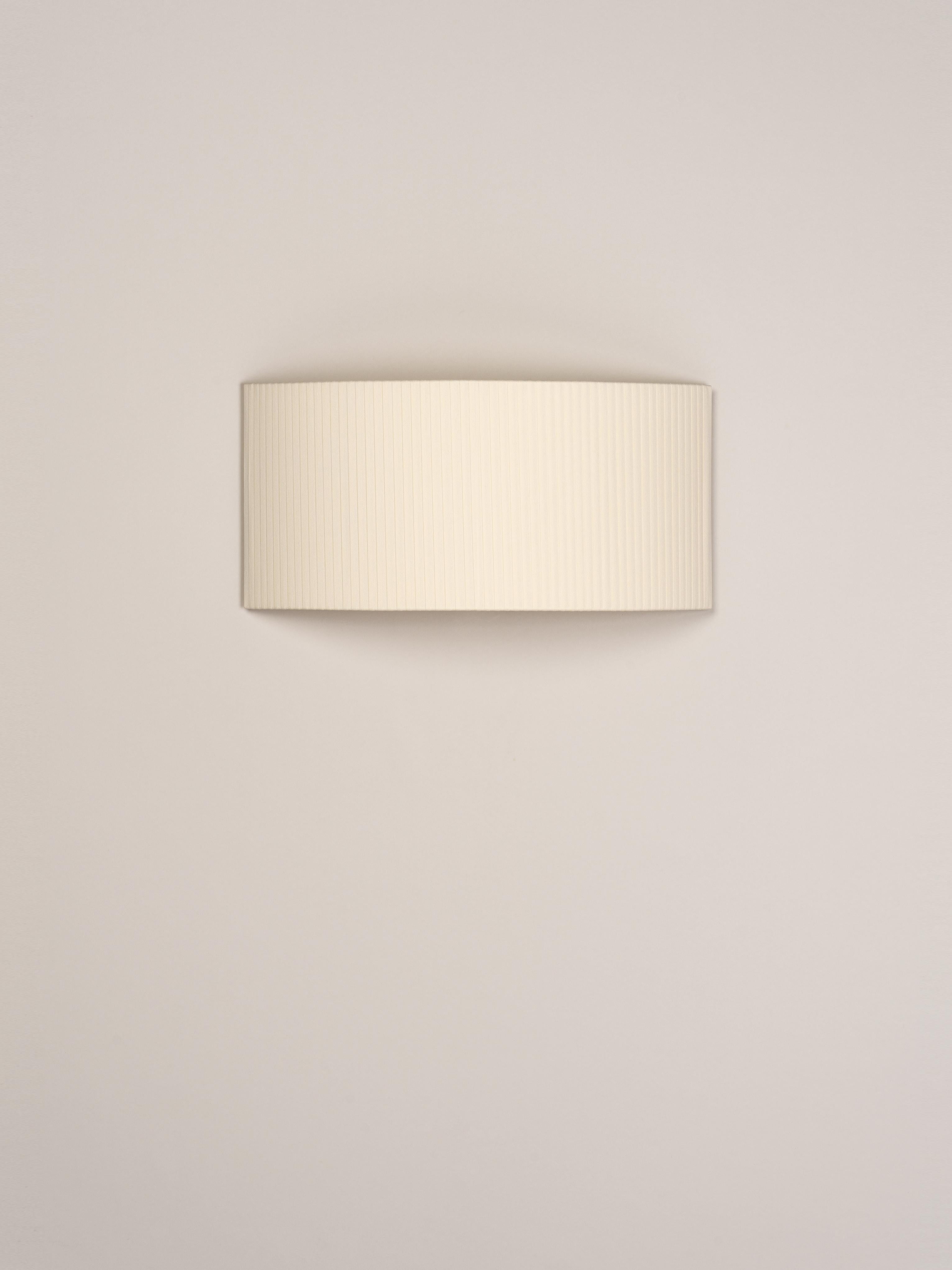Natural Comodín Rectangular wall lamp by Santa & Cole
Dimensions: D 50 x W 13 x H 24 cm
Materials: Metal, ribbon.

This minimalist wall lamp humanises neutral spaces with its colourful and functional sobriety. The shade is fondly hand-ribboned,
