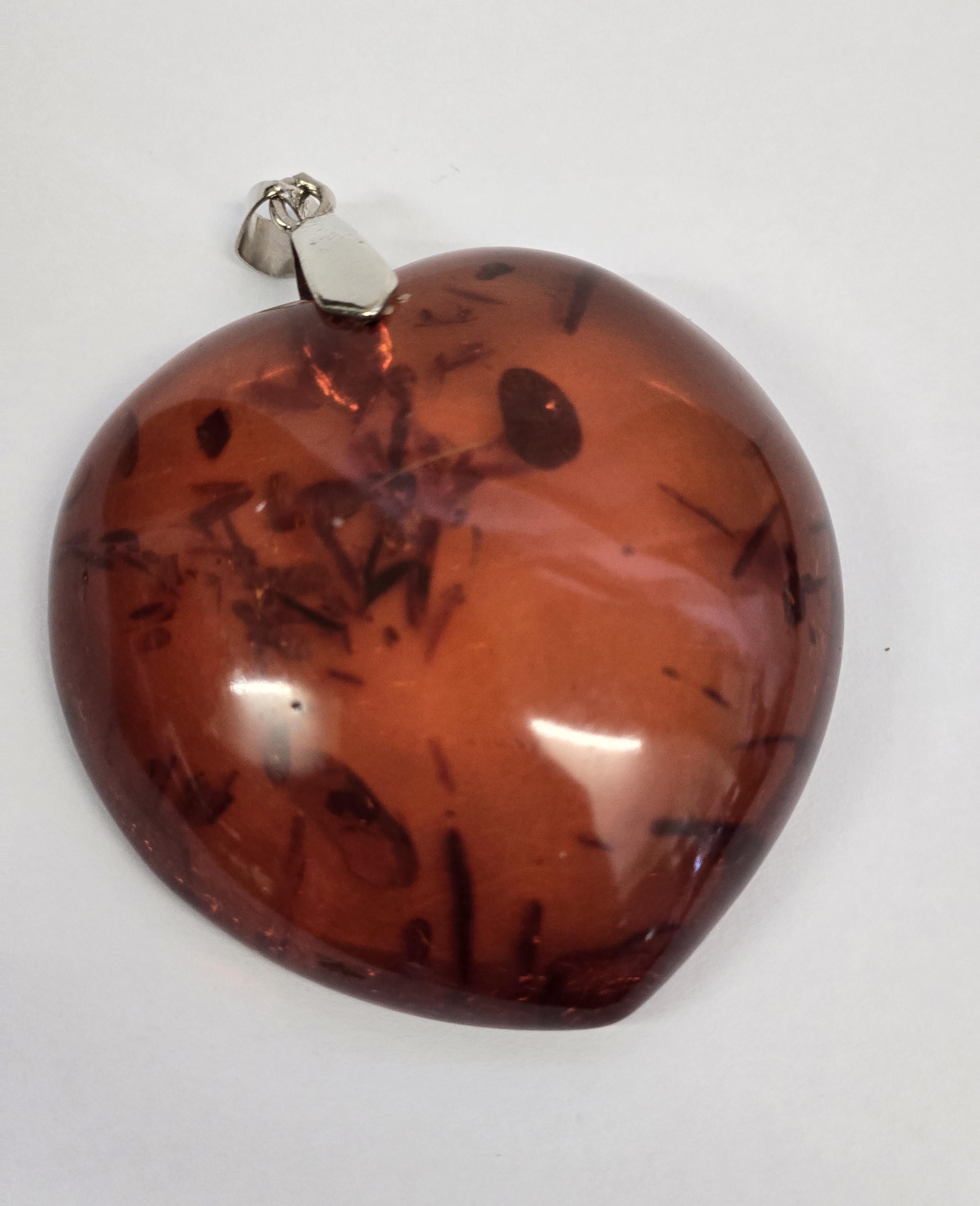 Questo ciondolo è finemente intagliato nell'ambra naturale color miele scuro, a forma di cuore senza tempo. La sua tonalità ricca e calda è evidenziata da una finitura liscia e lucida che esalta la bellezza organica della gemma. Le inclusioni