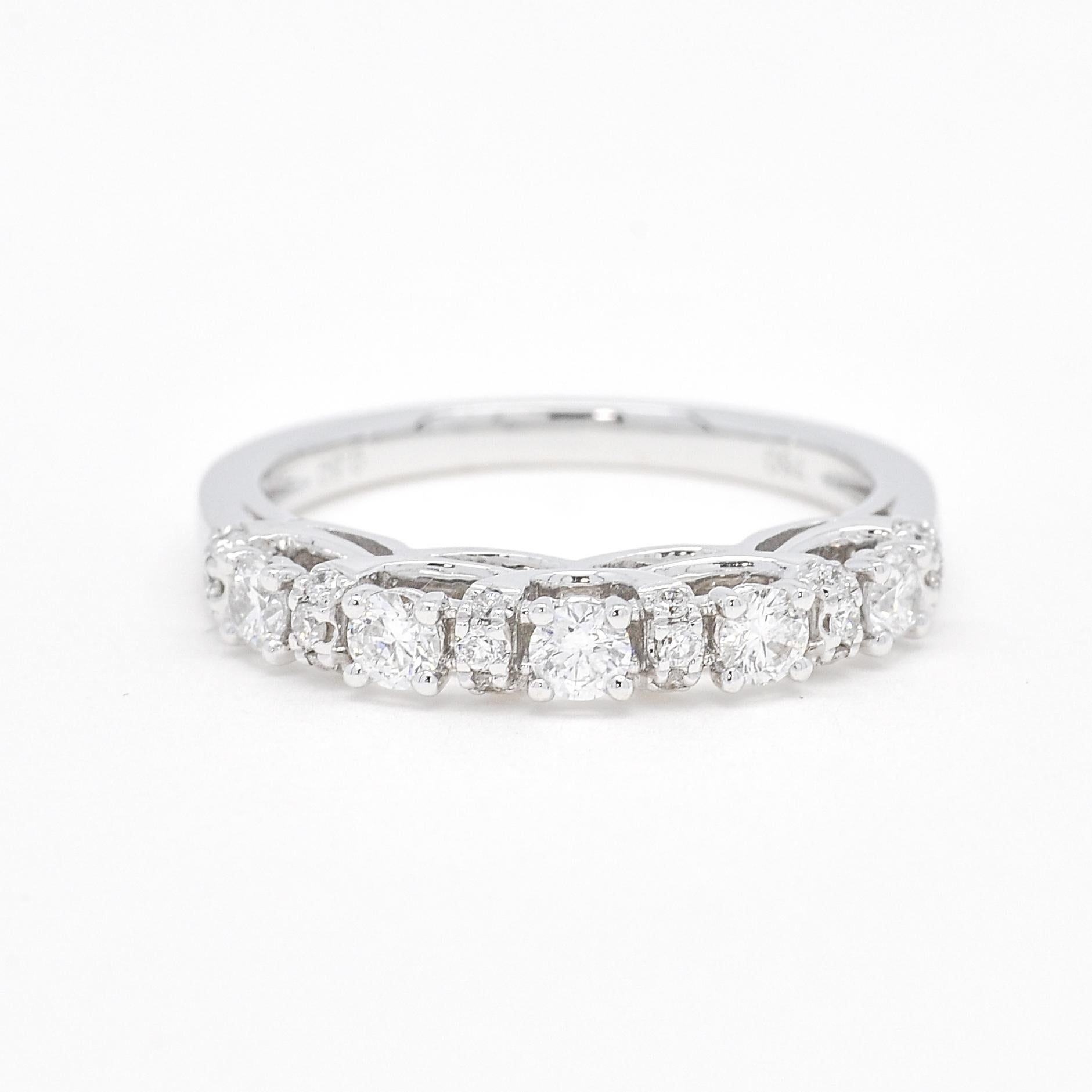 Celebra tu amor con estilo con este impresionante anillo de aniversario. Elaborado en lustroso oro blanco de 18 quilates, este diseño único presenta cinco piedras redondas engastadas en garras, combinadas con diamantes más pequeños engastados en