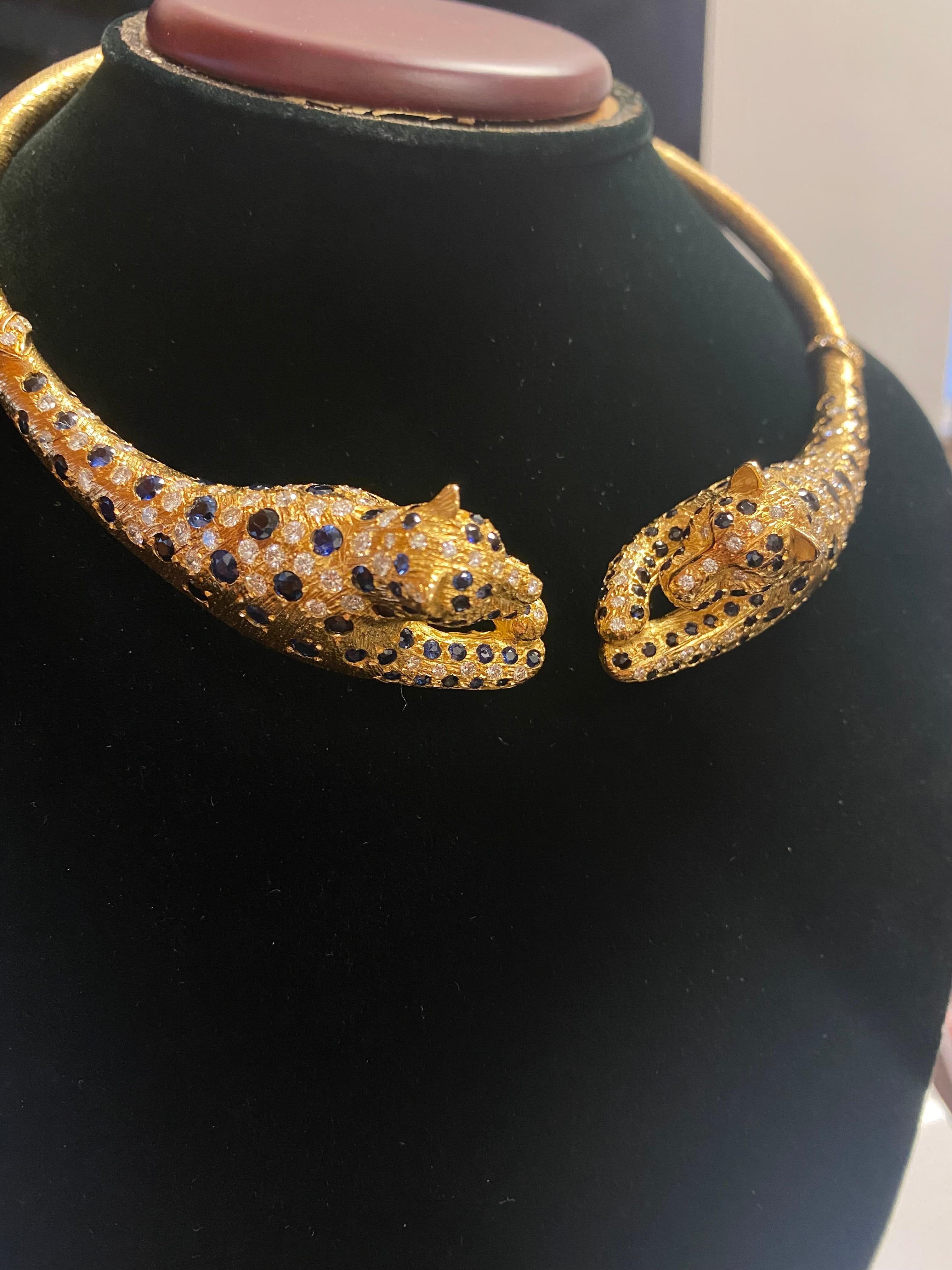 Diamond, sapphire, and 18K yellow gold spring-loaded choker necklace in a Cartier style with two leopards in a relaxed pose. This necklace features 120 natural diamonds of VS1 clarity/F-G color and 160 round cut blue sapphires. The necklace is
