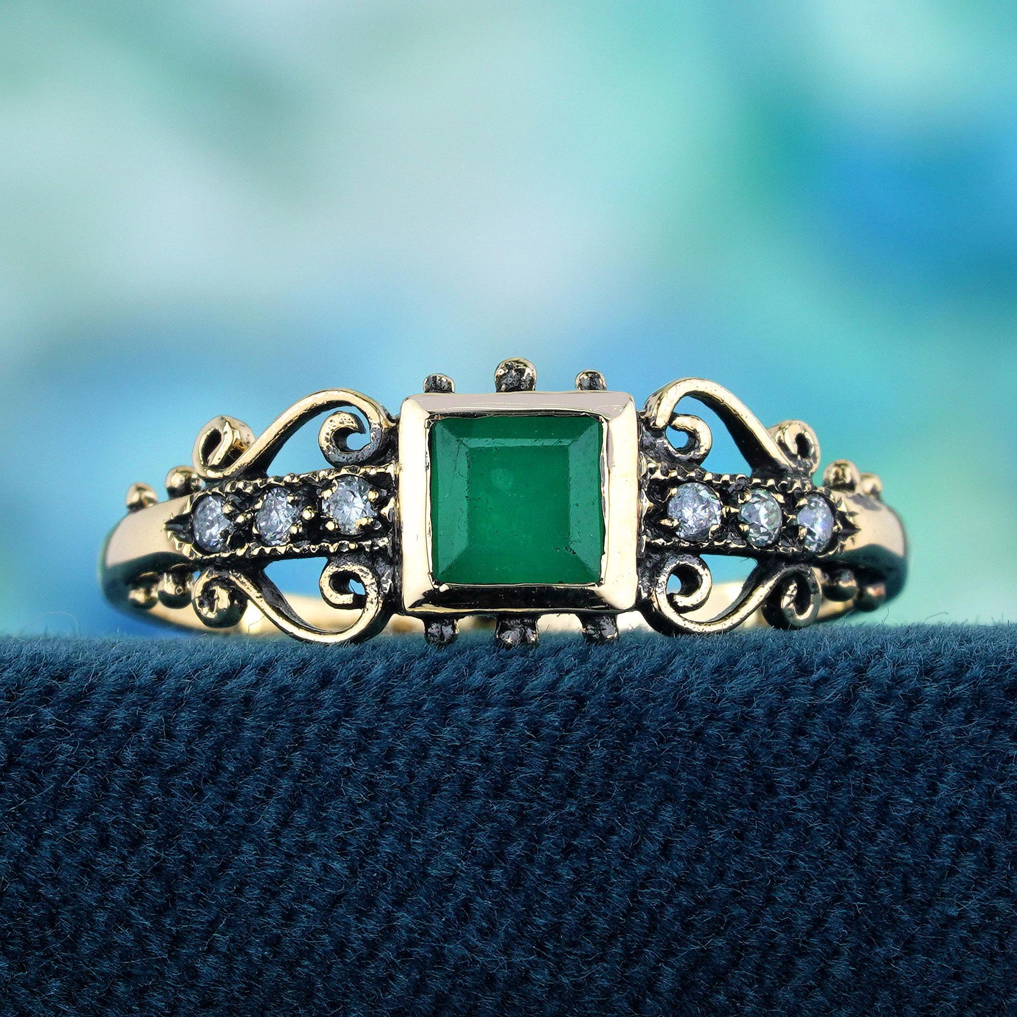 A central square emerald, faceted to showcase its rich green hue, takes center stage in this exquisite ring. Flanking the emerald are three small, round-cut diamonds embedded in the gold on each side. The yellow gold band features detailed filigree