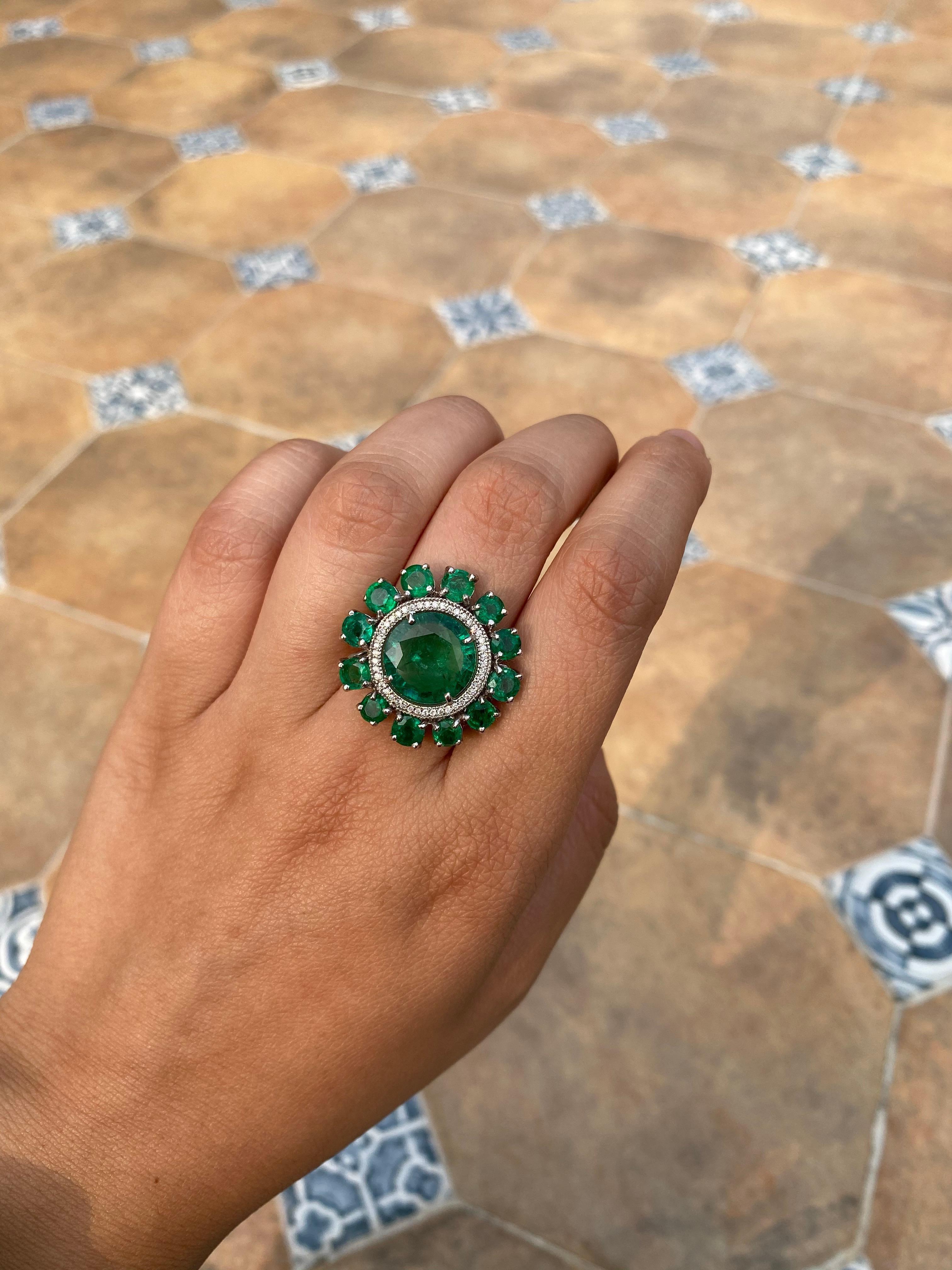 Ein wunderschöner und klassischer Ring mit rundem Smaragdschliff, gefasst in 18 Karat Weißgold mit Diamanten. Dieser wunderschöne Smaragdring hat einen 4,1 Karat schweren Mittelteil, der von kleineren 3,85 Karat Smaragden umgeben ist. Das Gewicht