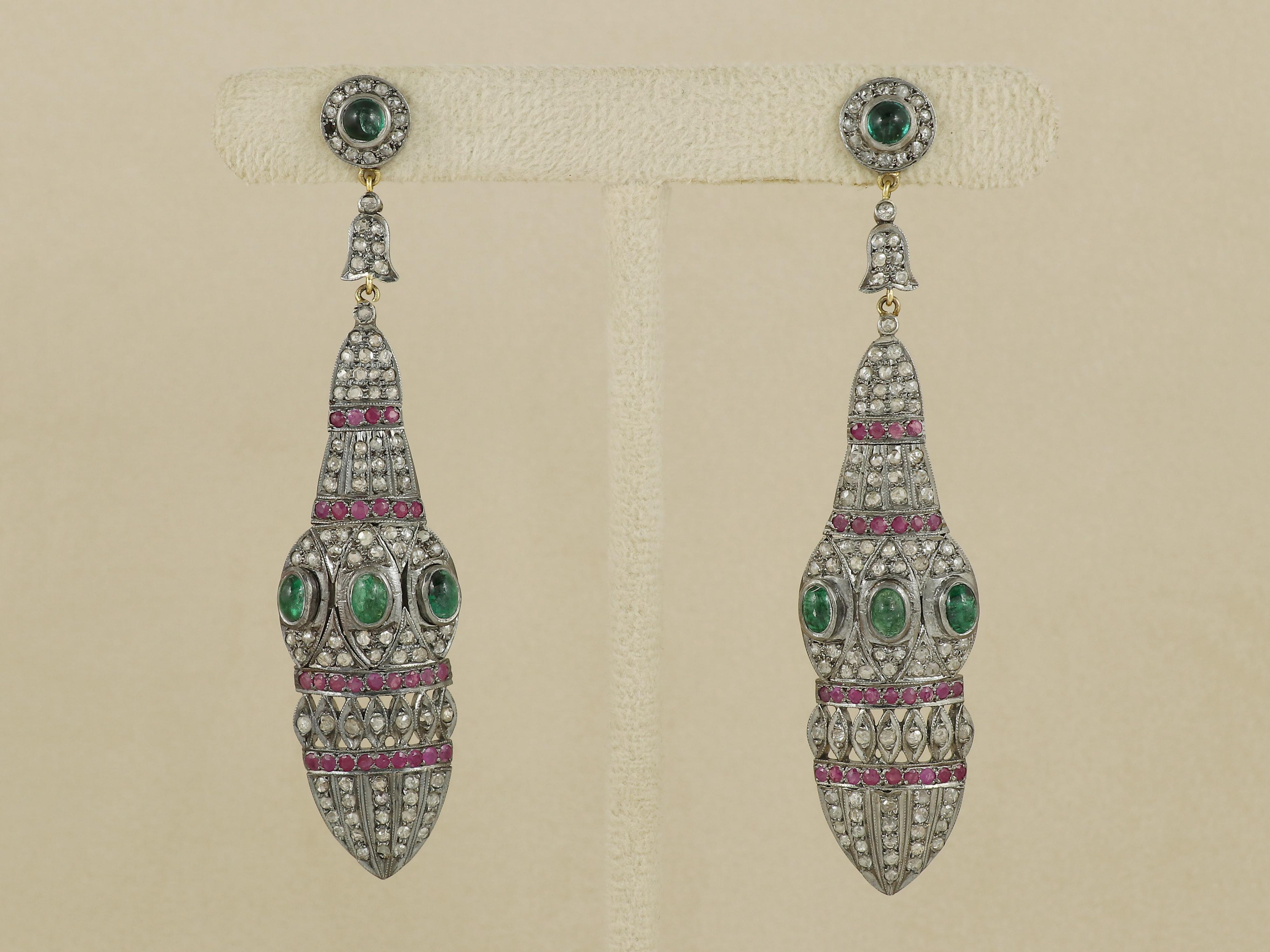 Magnifica incarnazione dell'eleganza vittoriana, questi orecchini penzolanti presentano un contrasto armonioso di colori lussureggianti e metalleria antica. Il design inizia con un affascinante smeraldo rotondo incastonato saldamente nella parte