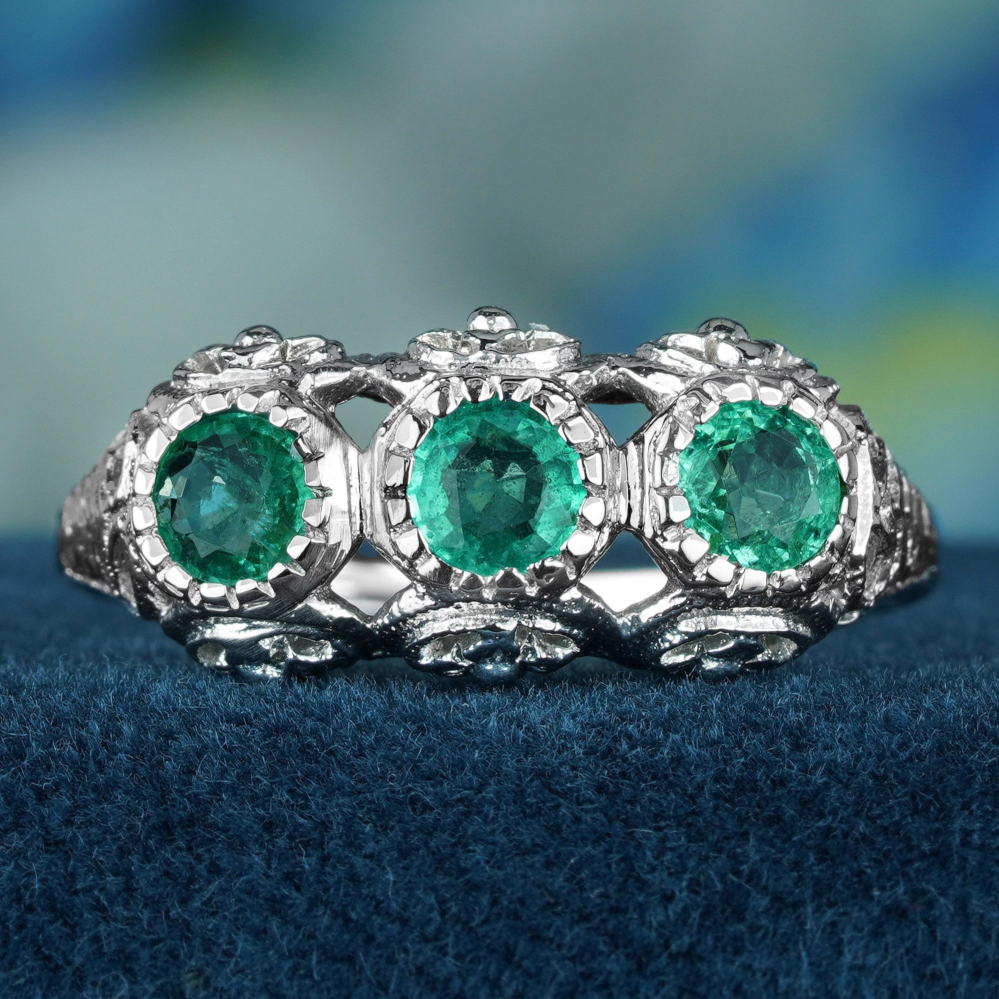 The antique style white gold ring glimmers reminiscent of moonlight glistening on snow, with the detailed filigree winding around the three emeralds like celestial lace woven by starlight. The trio emeralds, a captivating visual feast, display lush