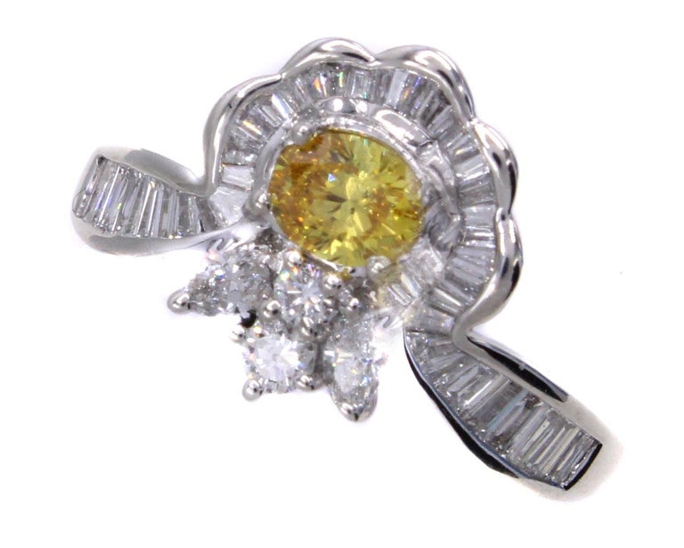 Centrally set with a natural fancy vivid orange-yellow oval brilliant diamond and embellished by perfectly matched bright white baguette and marquis cut diamonds, this ring brings out a beautiful contrast of brilliance and color. The fancy vivid is