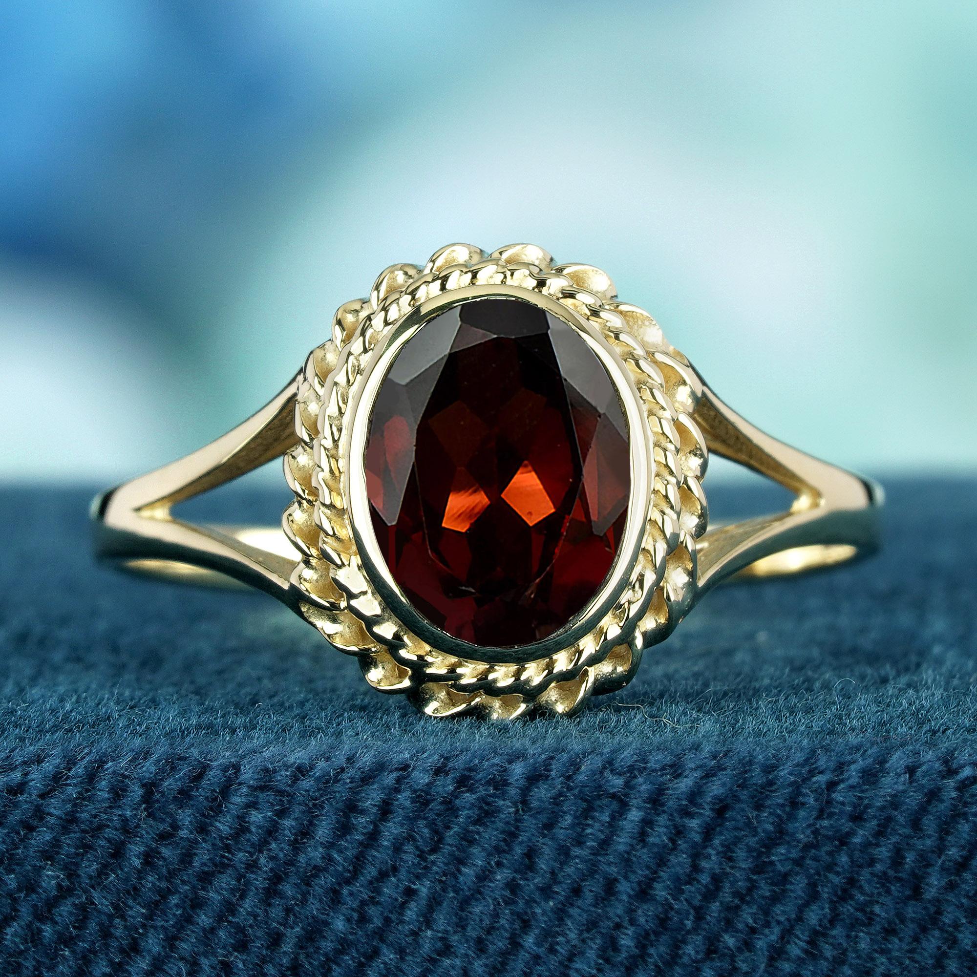 This vintage-inspired split shank ring boasts a captivating twisted rope design, delicately enveloping the entire yellow gold band and seamlessly encircling the oval deep read garnet at its center. This intricate detailing not only adds a unique