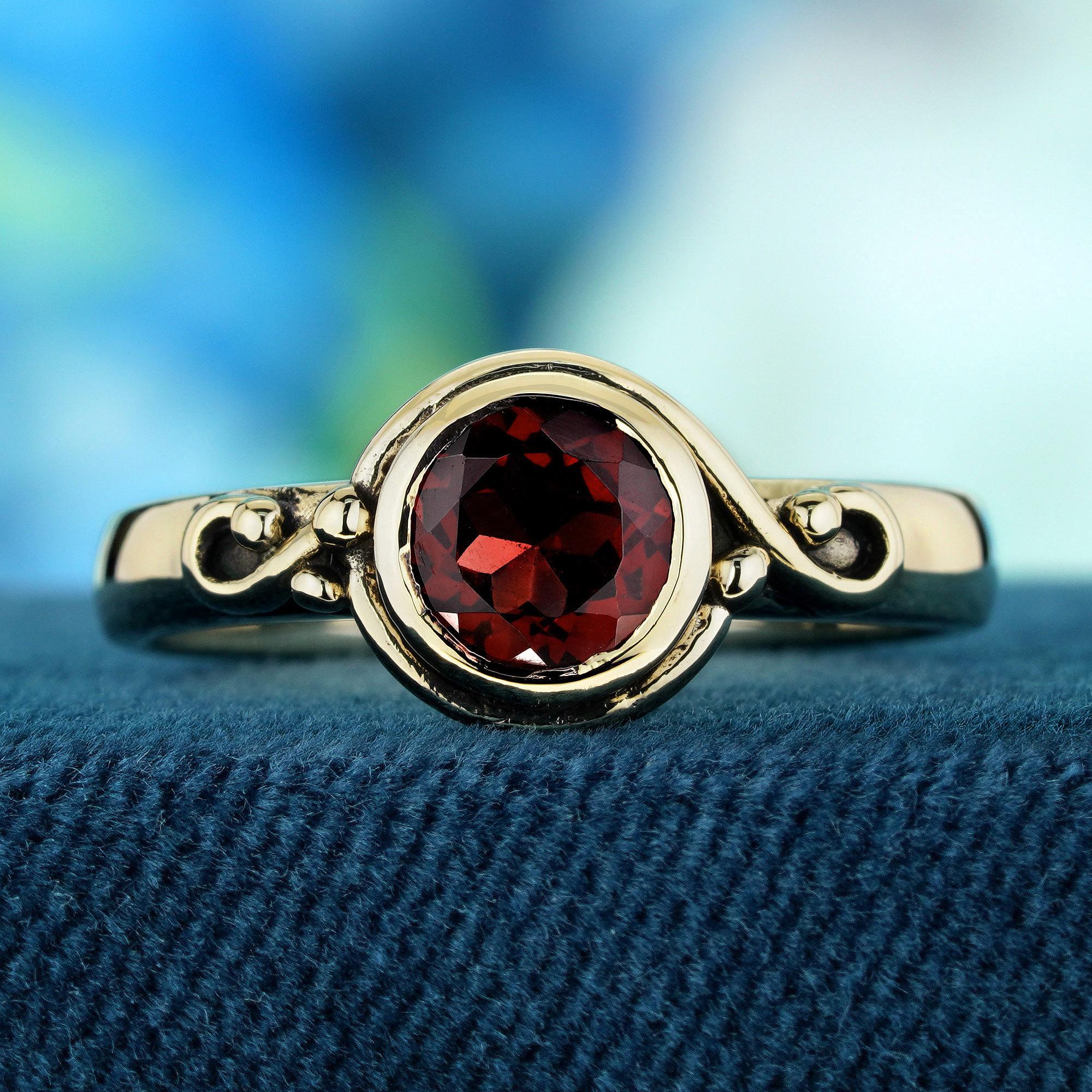 Eleva tu mano con un toque delicado y distintivo con este anillo de estilo vintage en oro amarillo. Centrada con un granate redondo en un engaste de bisel, que emite un rico tono rojo, esta pieza destila sofisticación. La banda, adornada con