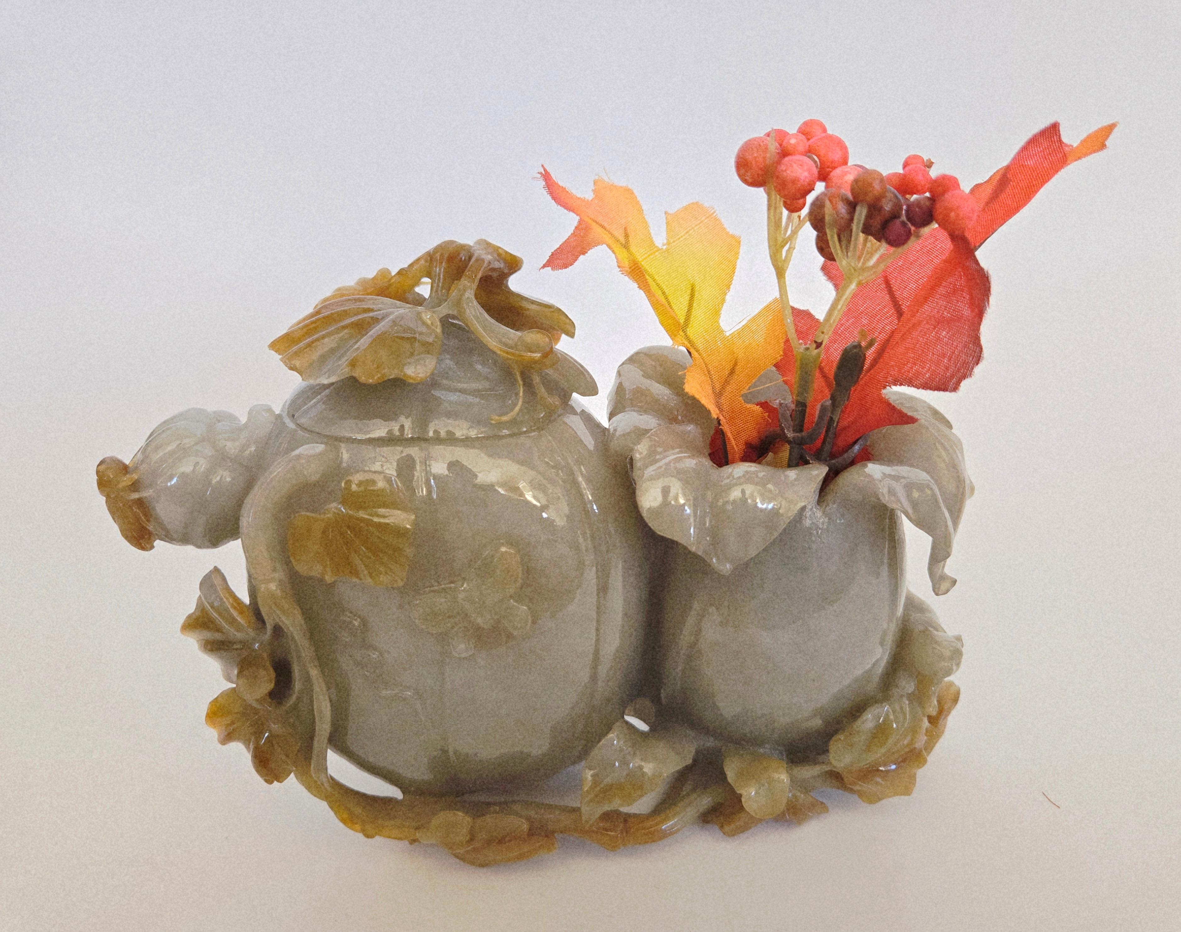 This exquisite piece is a natural gray green and brown jadeite jade carving, handcrafted in the form of pumpkins surrounded by delicate pumpkin vines. The sculpture features finely detailed depictions of a butterfly, a cricket, and a mouse resting