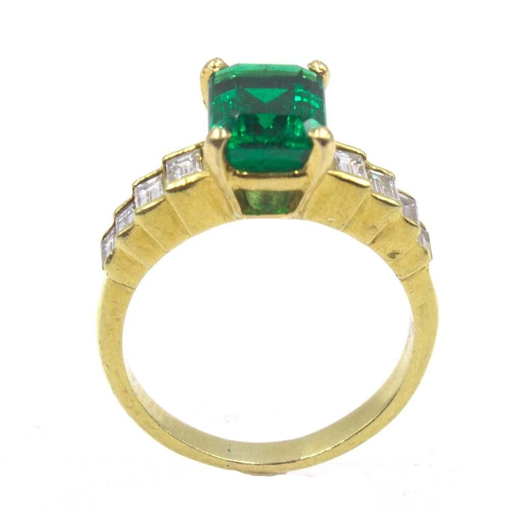 Beautiful green emerald and diamond ring in an 18 karat yellow gold setting. The octagonal step cut 2.39 carat emerald is certified by the GIA. It is F2 clarity, and measures 9 x 6.8 x 5mm.  There are 8 baguette cut diamonds that equal .80 carat