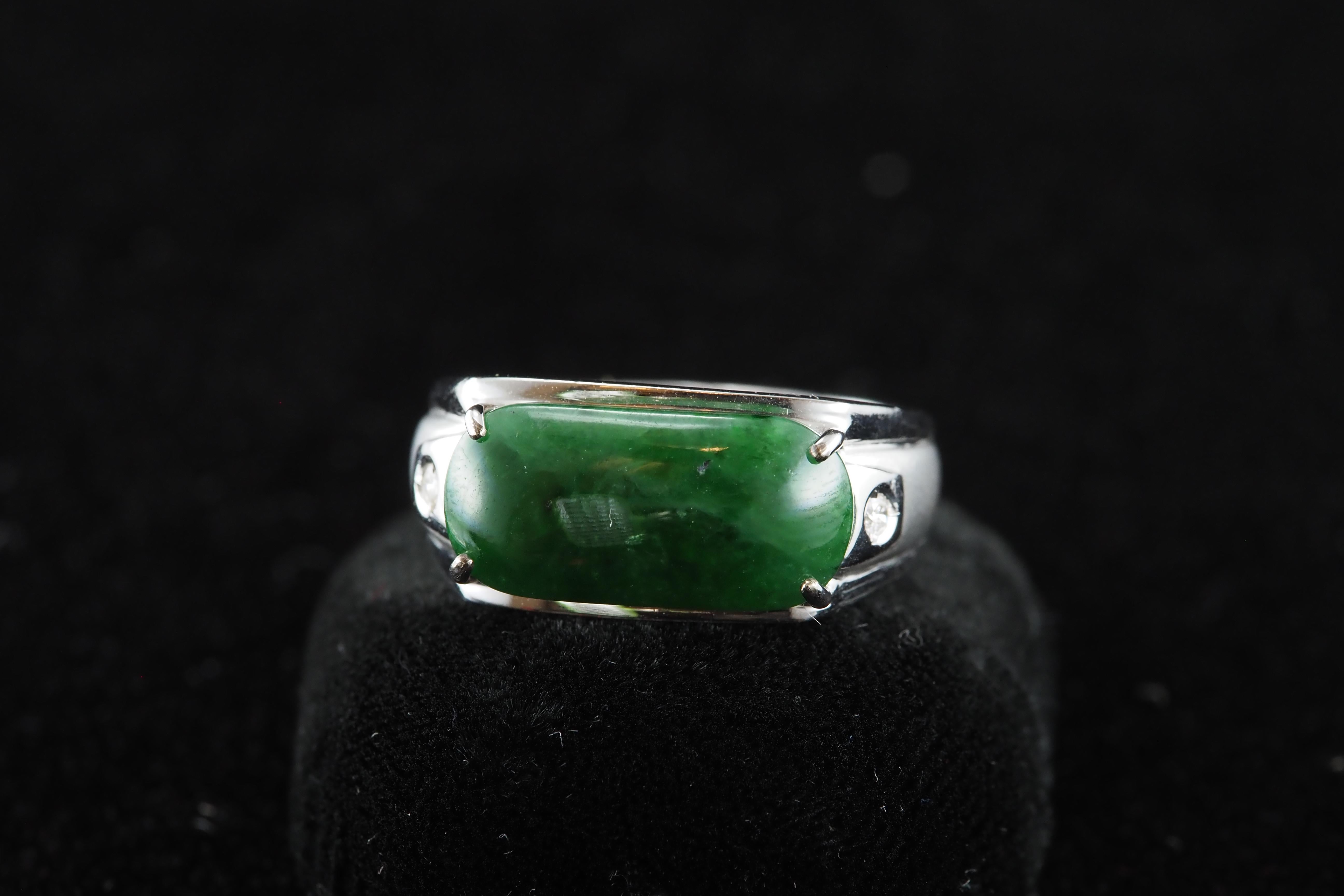 This exquisite ring showcases a natural rectangular dark green jade of rich, even color, measuring approximately 1.7 cm in height and 0.9 cm in width. It is gracefully accented by two natural diamonds on either side, enhancing the piece’s timeless