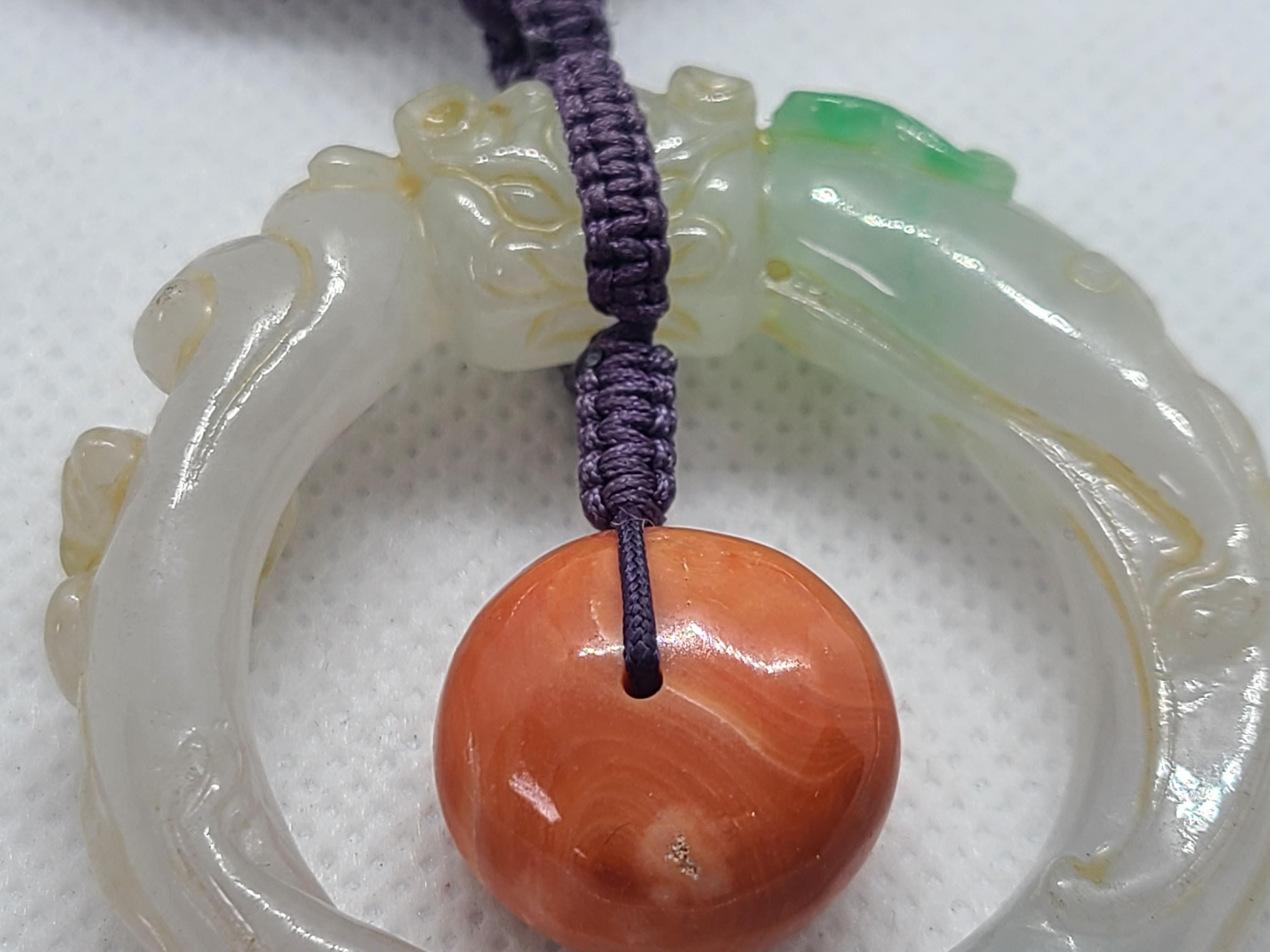 Collana fatta a mano con uno squisito braccialetto di giada verde chiaro, marrone e grigio intricatamente scolpito con una vecchia testa di drago tra nuvole vorticose. Il centrotavola è completato da una perla di corallo naturale antico, che crea
