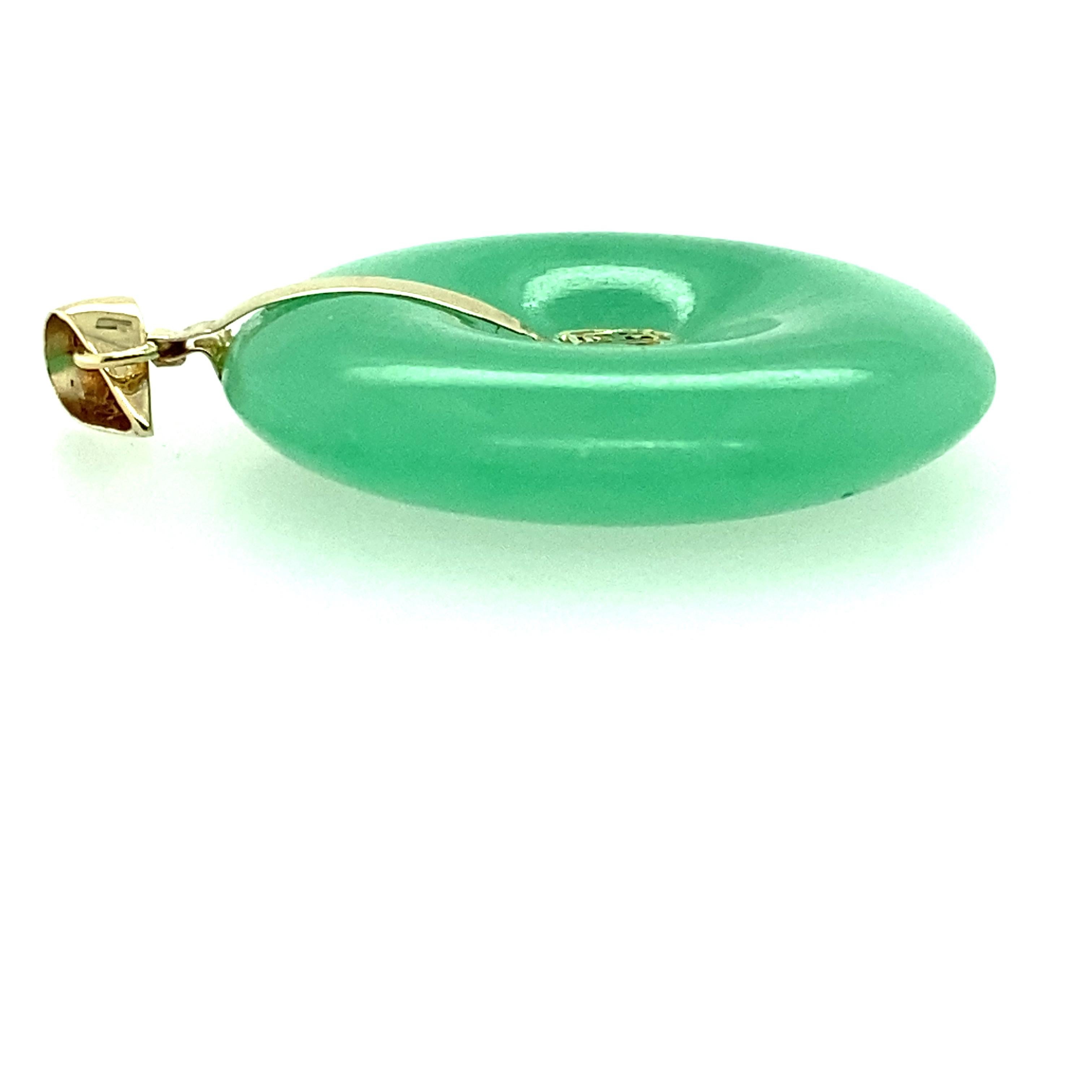 One 14 karat yellow gold natural jade disc pendant measuring one inch in diameter and 5.15mm wide.  