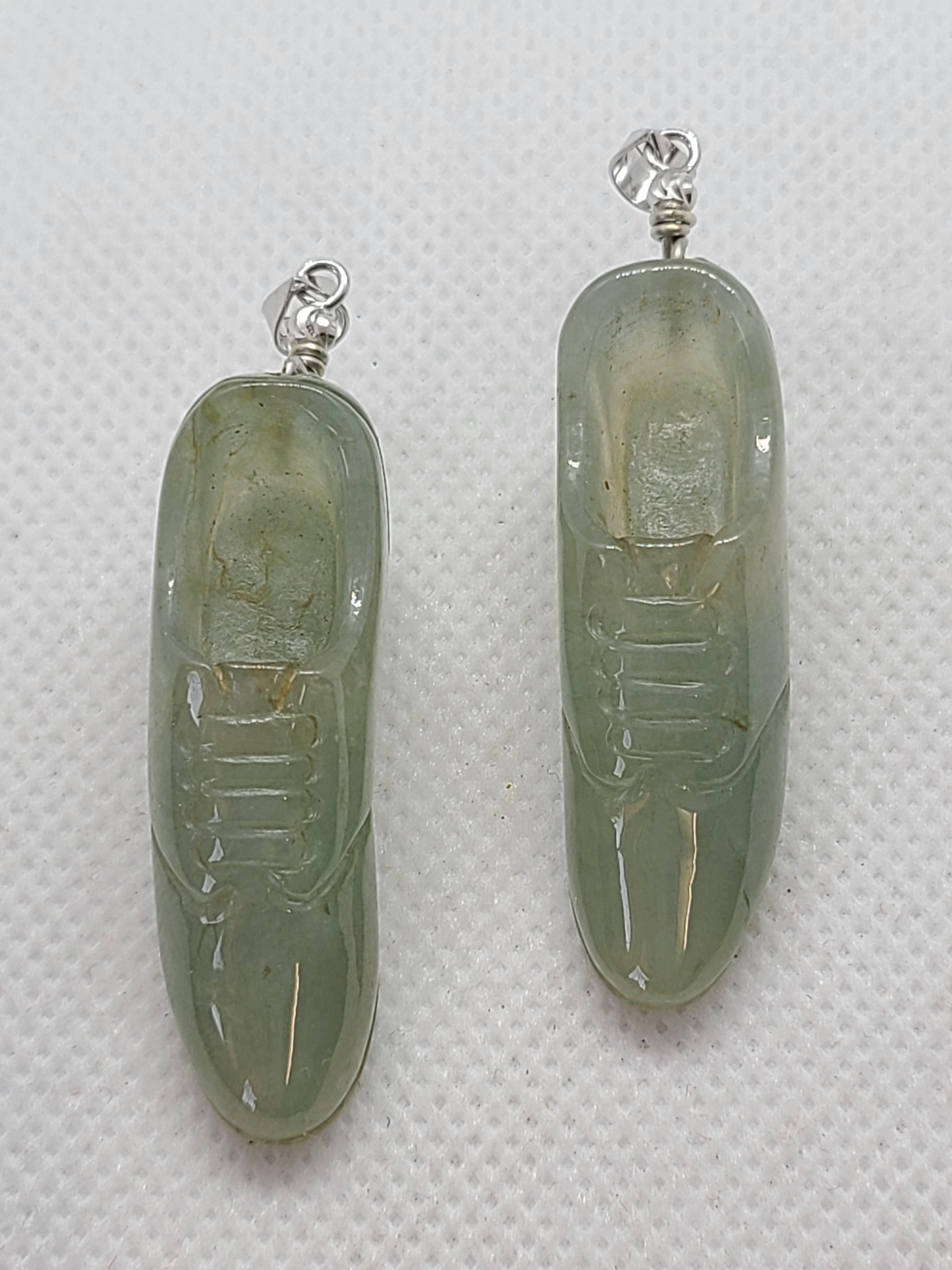 Paire de pendentifs en jade naturel, sculptés de manière complexe en forme de chaussures, chacun mesurant environ 4,3 x 1,2 x 1,2 cm. Ce charmant duo symbolise l'harmonie en mouvement et l'élégance intemporelle. 