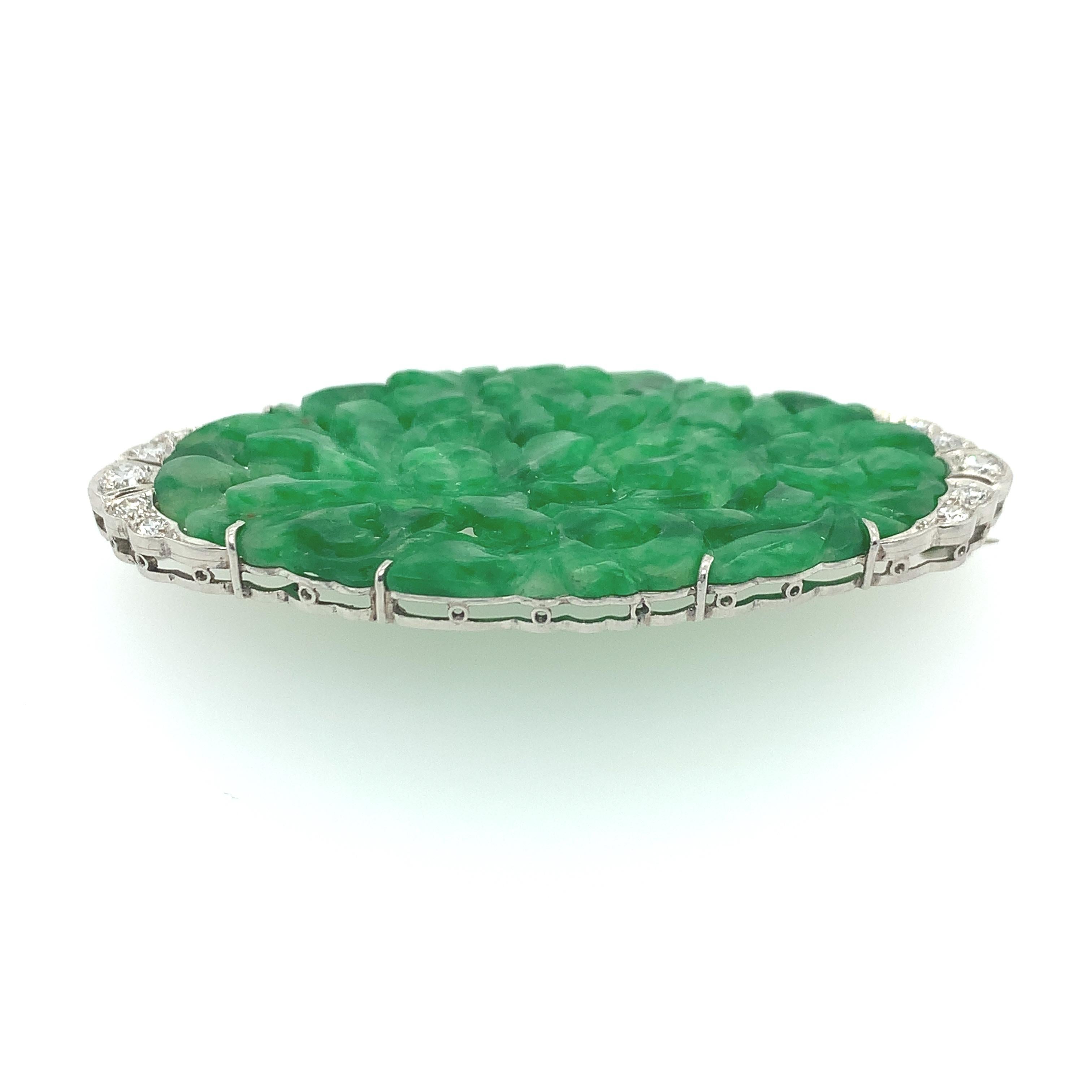 Intricately carved natural jadeite brooch with floral design accented with (10) ten total round brilliant cut near-colorless diamonds weighing approximately 0.36 carats. This glamorous translucent brooch includes a platinum frame, and its stunning
