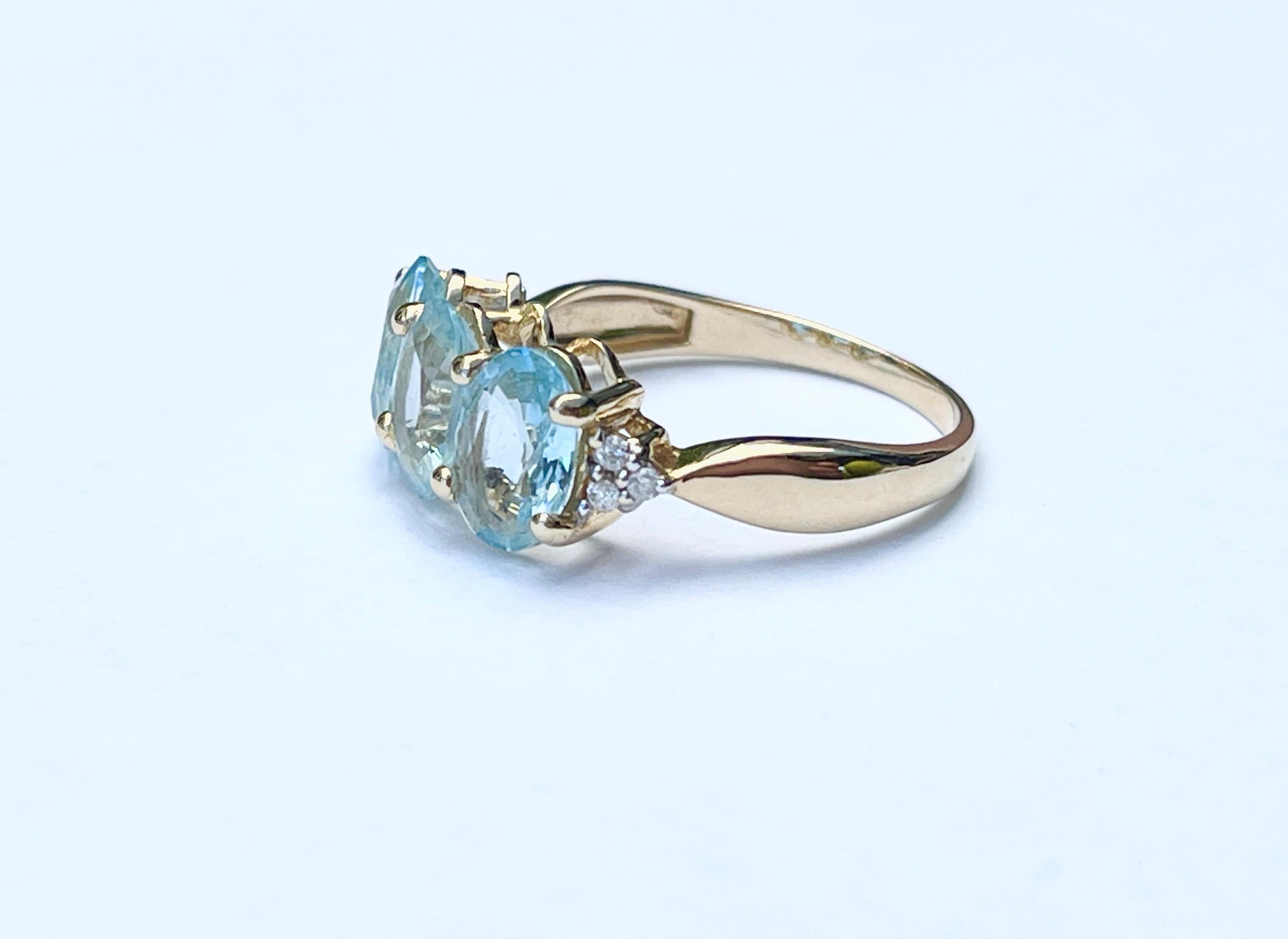 Dieser wunderschöne Ring ist mit 3 Aquamarinen im Ovalschliff und kleinen Diamanten in 9 Karat Gelbgold besetzt. 
Der Aquamarin hat eine relativ helle Farbe und eine sehr gute Klarheit.  Zusammen wiegen sie etwa 0,70ct.
Auf den Schultern befinden