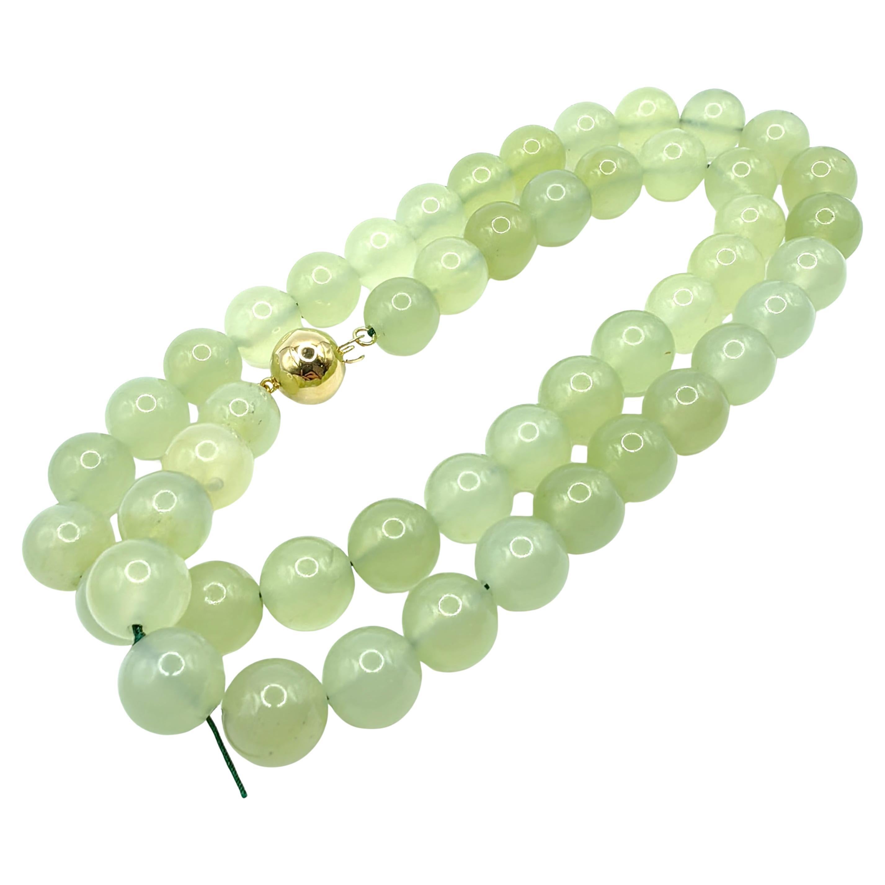 Timeless and sophisticated, this exquisite necklace features a strand of natural light green serpentine jade beads in a soft, luminous hue. Each 10mm bead is meticulously polished to showcase the stone's smooth texture and subtle variations in