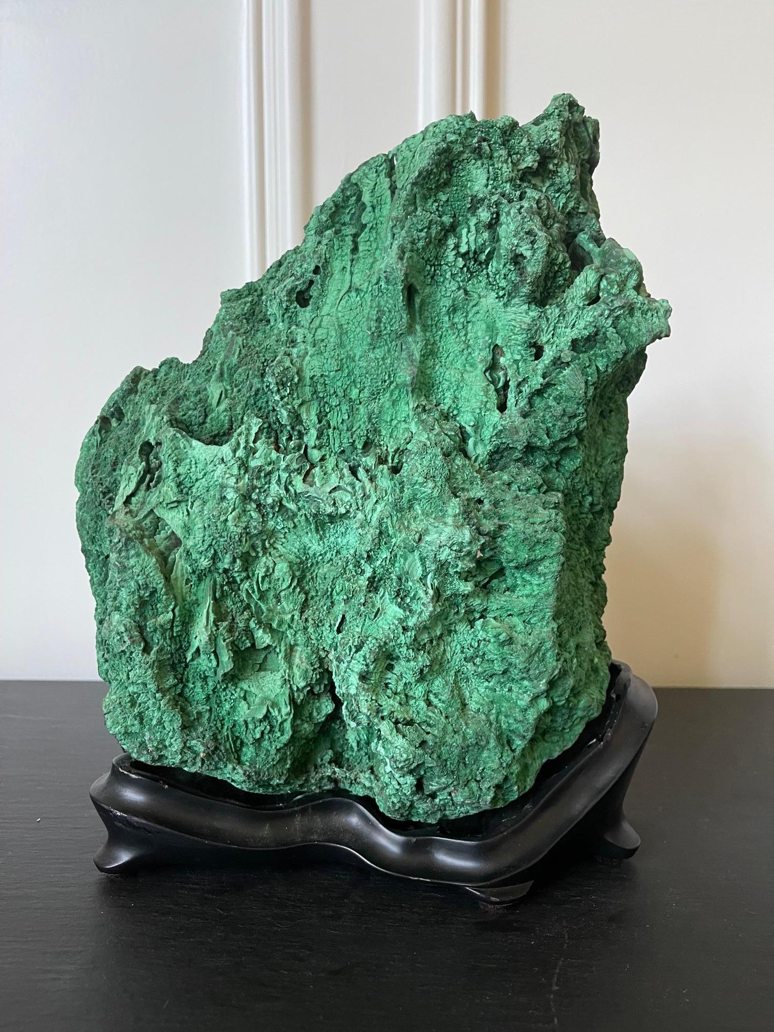 A natural malachite boulder on a fitted wood stand displayed as a Chinese scholar stone (Gong Shi), also known as meditation stone. The natural gem specimen displays a wonderful mountainous form with a peak off the center, organic and well balanced.