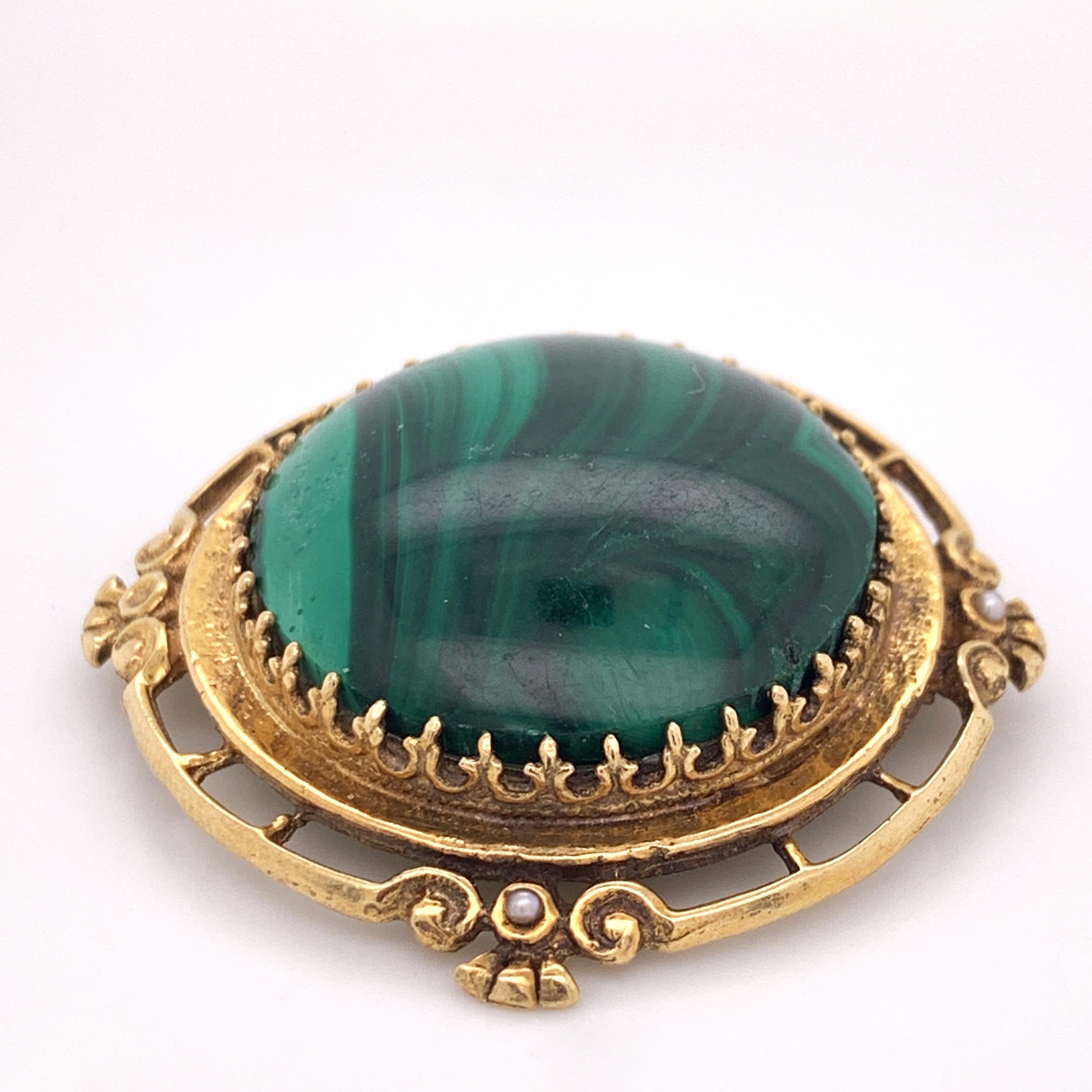 This gorgeous statement brooch is versatile and can also be worn as a pendant. It features a stunning natural malachite cabochon stone surrounded by a luxurious gold filigree frame that is adorned by 3 small seed pearls. The soft transcendent pearls