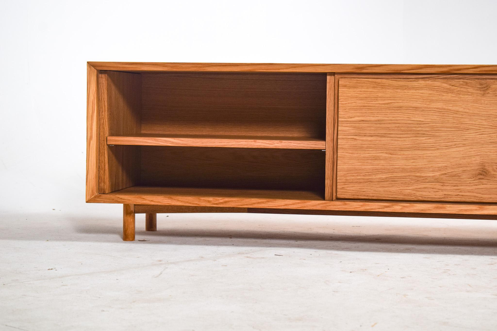 This elegant low-profile sideboard features a minimalist design crafted from pure oak wood with a warm, natural oil finish that highlights its rich grain pattern. It includes two sliding doors for concealed storage, combining functionality with