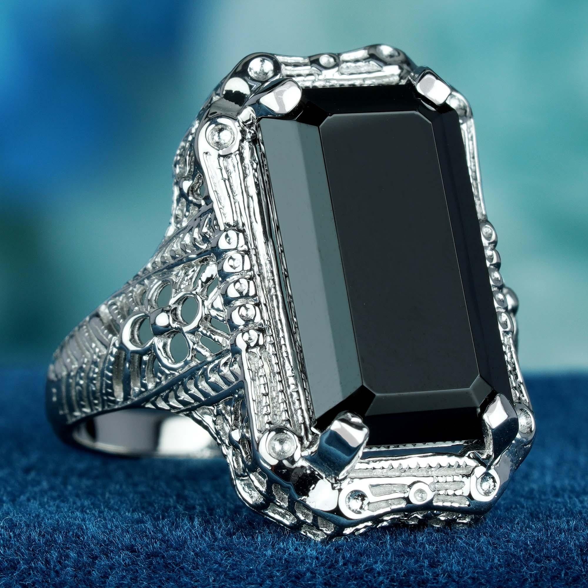 This ring is a truly exquisite piece of jewelry. The band, crafted from solid white gold adorned with a delicate filigree design that is reminiscent of vintage lace features a mesmerizing emerald-cut black onyx gemstone that weighs a full 10 carats.