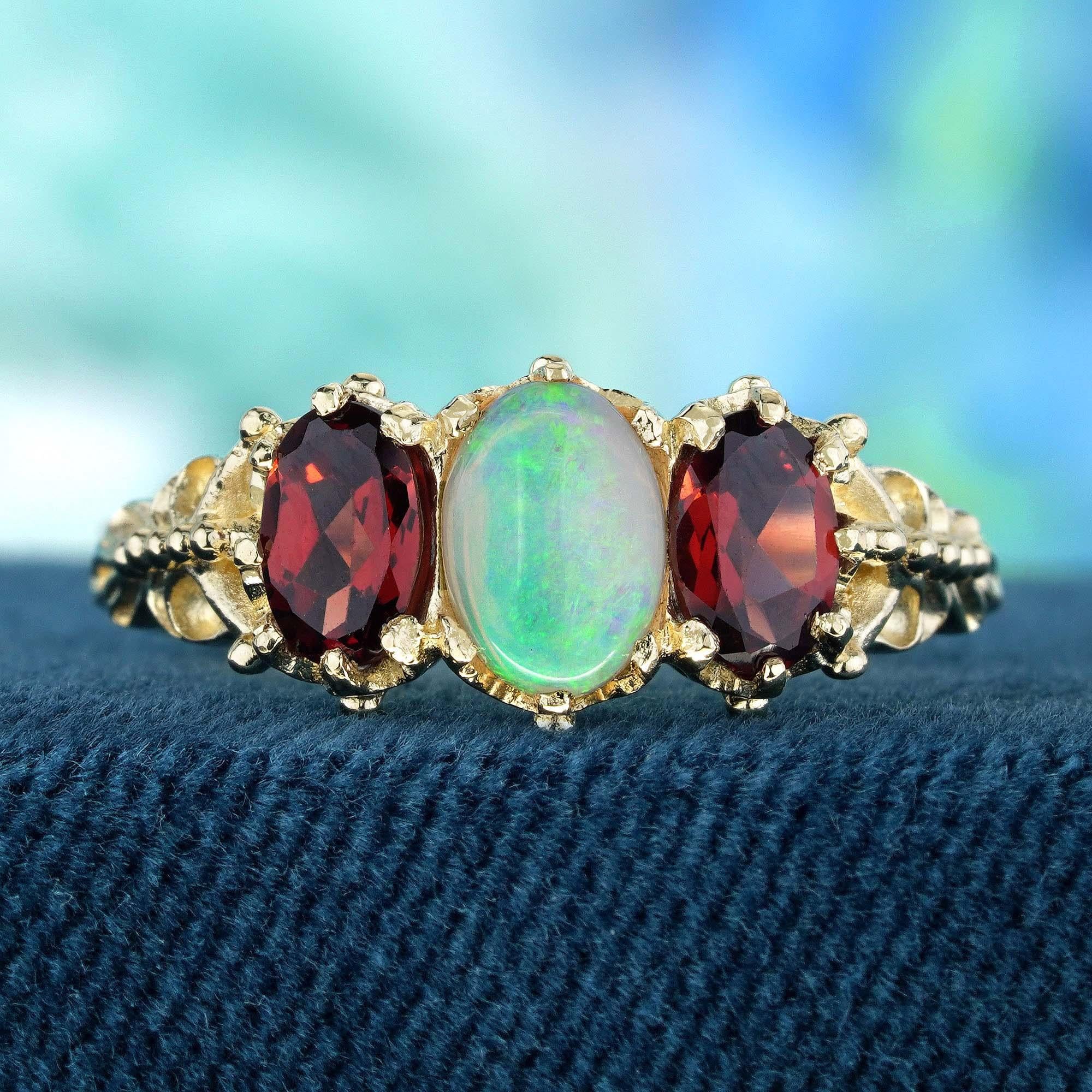 Cette bague met en valeur trois pierres naturelles, une opale ovale au centre, flanquée de grenats rouges ovales en serti clos, ce qui permet de capter la lumière et d'attirer les regards. L'anneau méticuleusement réalisé en or jaune avec de