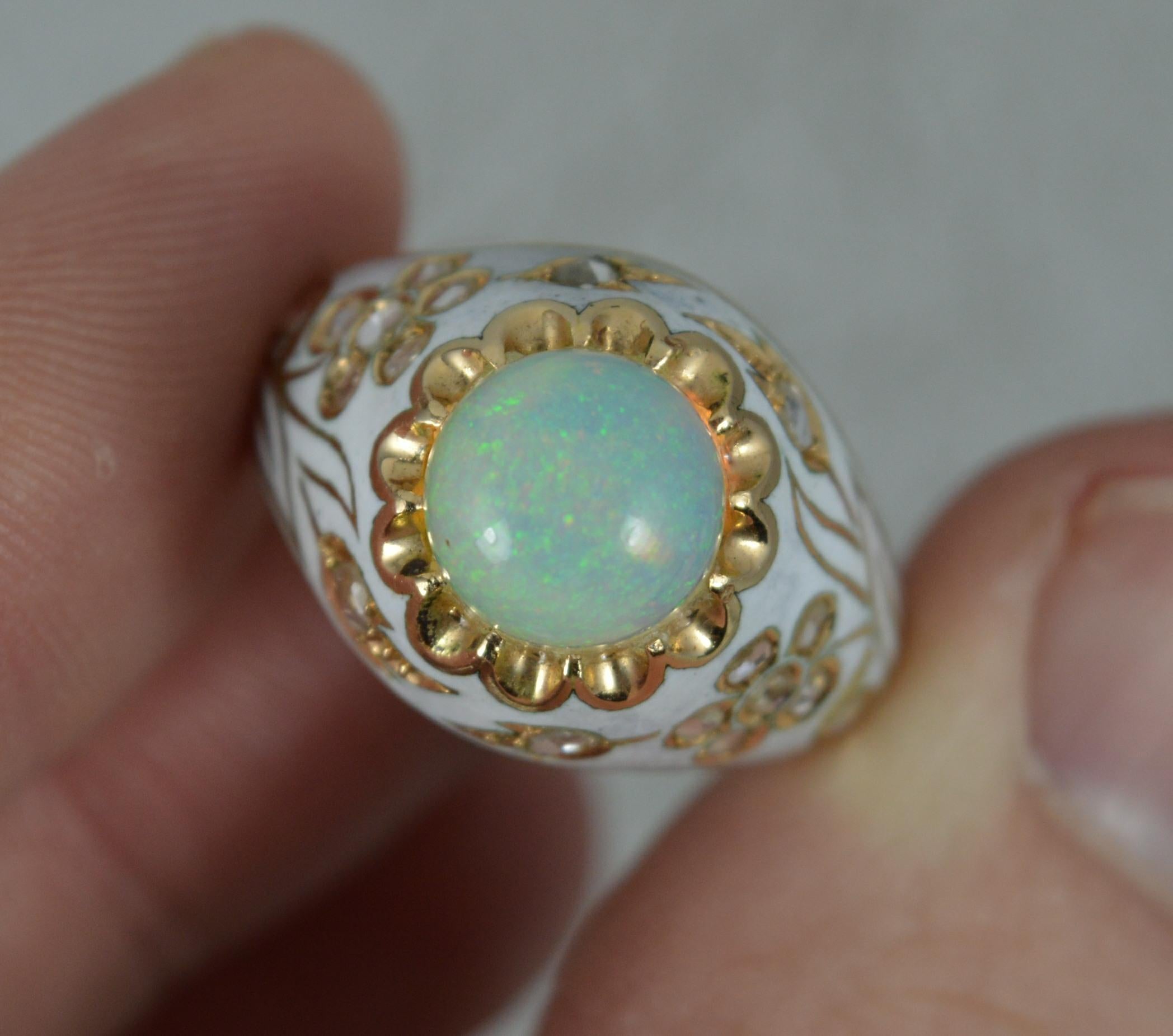 A stunning Opal, Diamond and Enamel ring.
Designed with a large circular natural opal of stunning colour. 8mm diameter.
Surrounding is a white enamel design with floral design including many natural rose cut diamonds.
14mm wide band to the