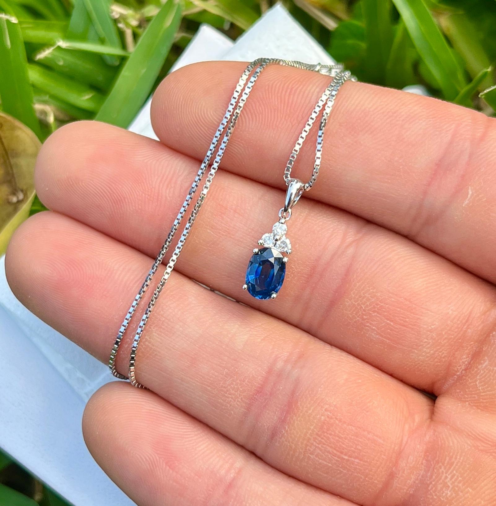 18-karat solid white gold drop pendant mounts a 1.20 carat natural Blue Sapphire. The pendant features a dynamic bail that connects 3 round-cut natural diamonds that form a triangle on the top. The Sapphire center stone is full of color, brilliance,